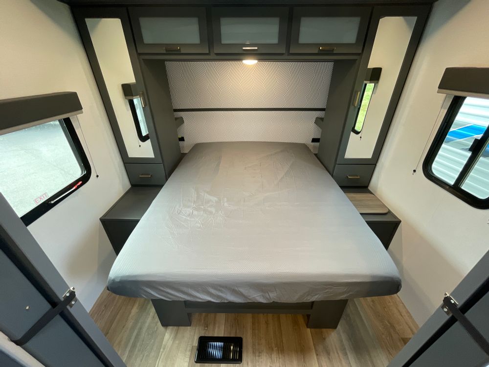 RV rental bedroom: a cozy space with a grey-sheeted bed, overhead cabinets, mirrored wardrobes, and windows.. Keystone RV Bullet Ultra Lite 2023
