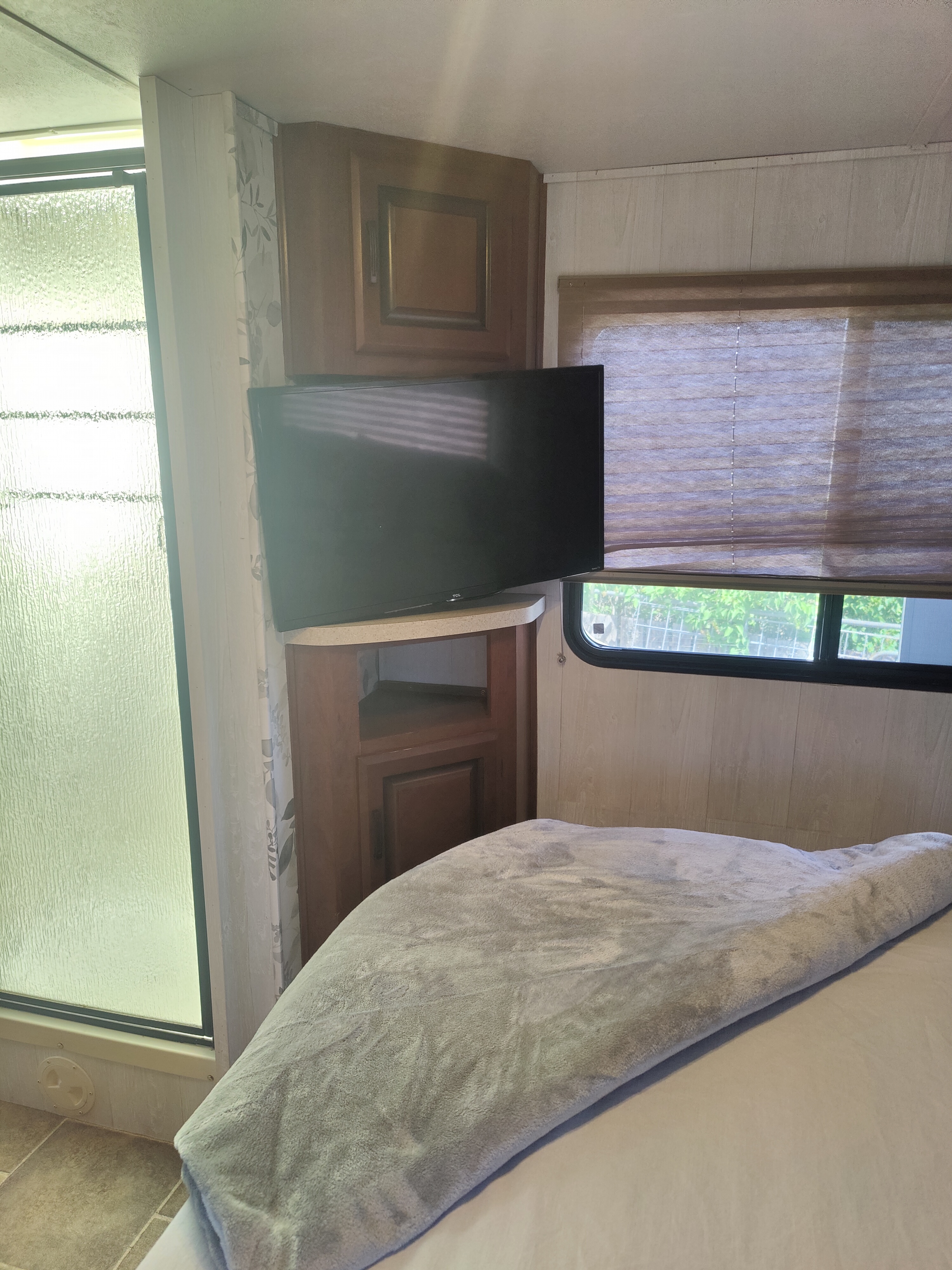 Inside an RV rental: functional bedroom area features a TV, corner cabinet, bed, window, and nearby shower.. Forest River Sunseeker 2012