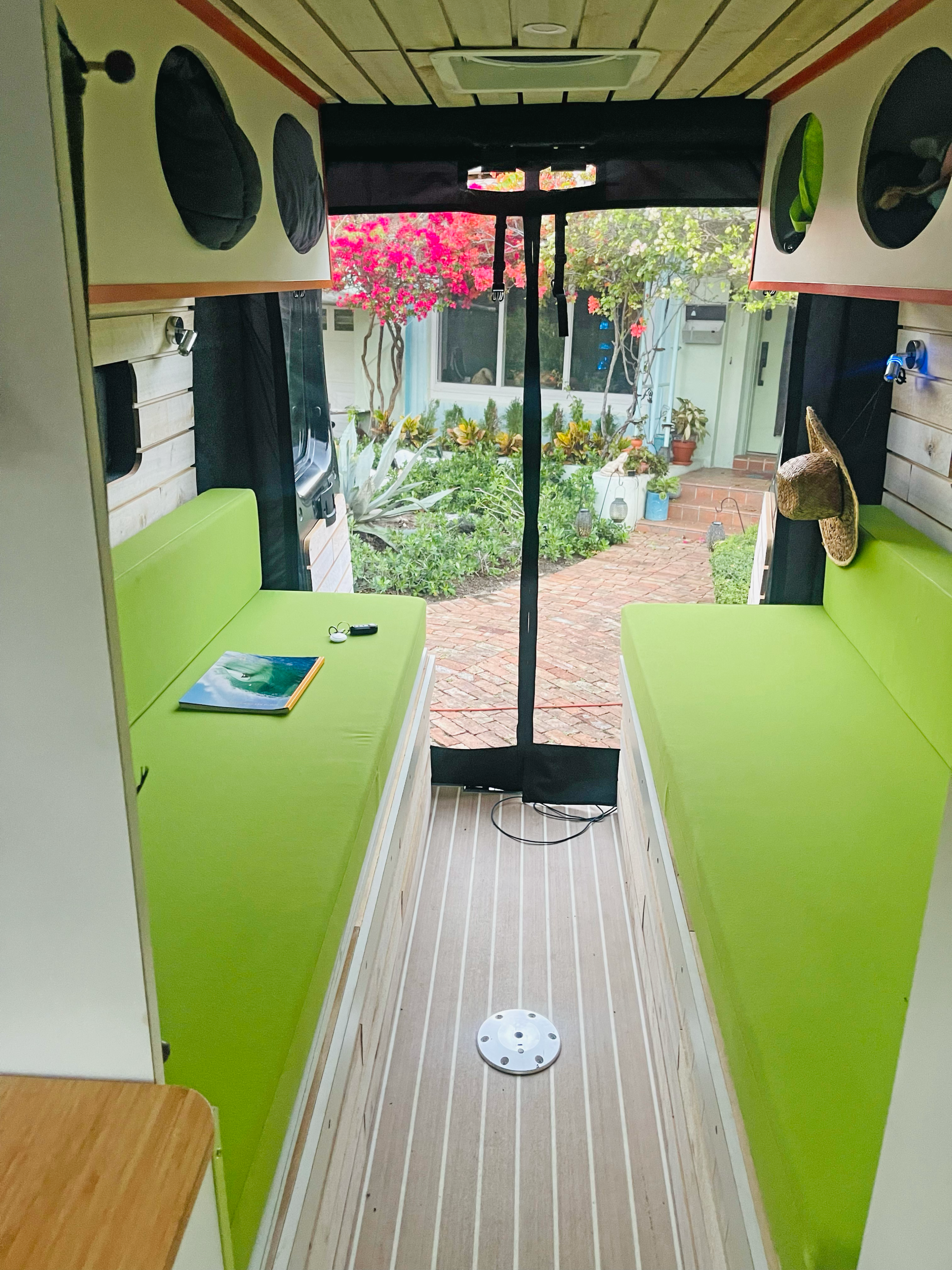 Vibrant green benches and wood-plank floor inside an RV rental, with a clear view of a beautiful outdoor garden.. Dodge Ram Van Roadtrek 2019