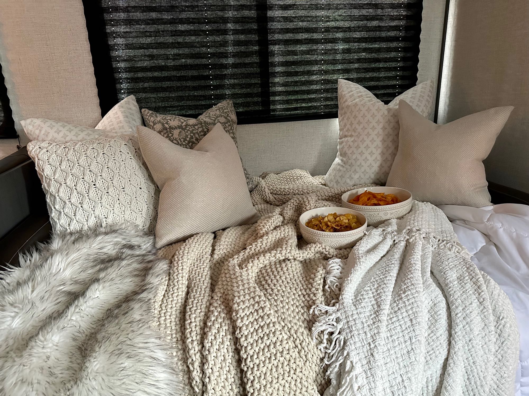 Cozy RV rental bed with layered pillows, textured blankets, and snacks for a relaxing break.. Dutchmen Aspen Trail 2022