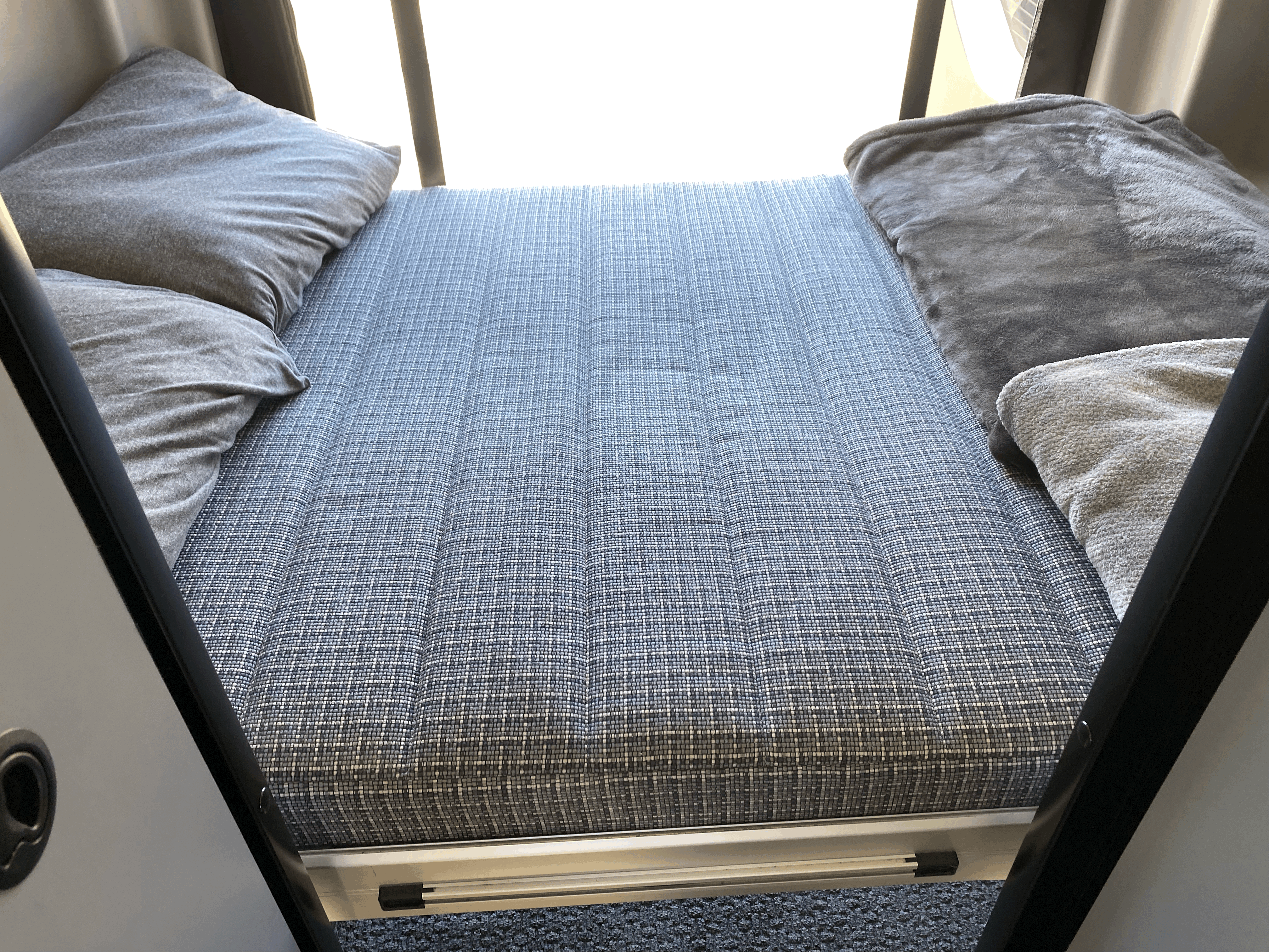 Cozy RV rental sleeping area featuring a patterned mattress, soft pillows, and blankets for comfortable travel.. Winnebago Revel 2023
