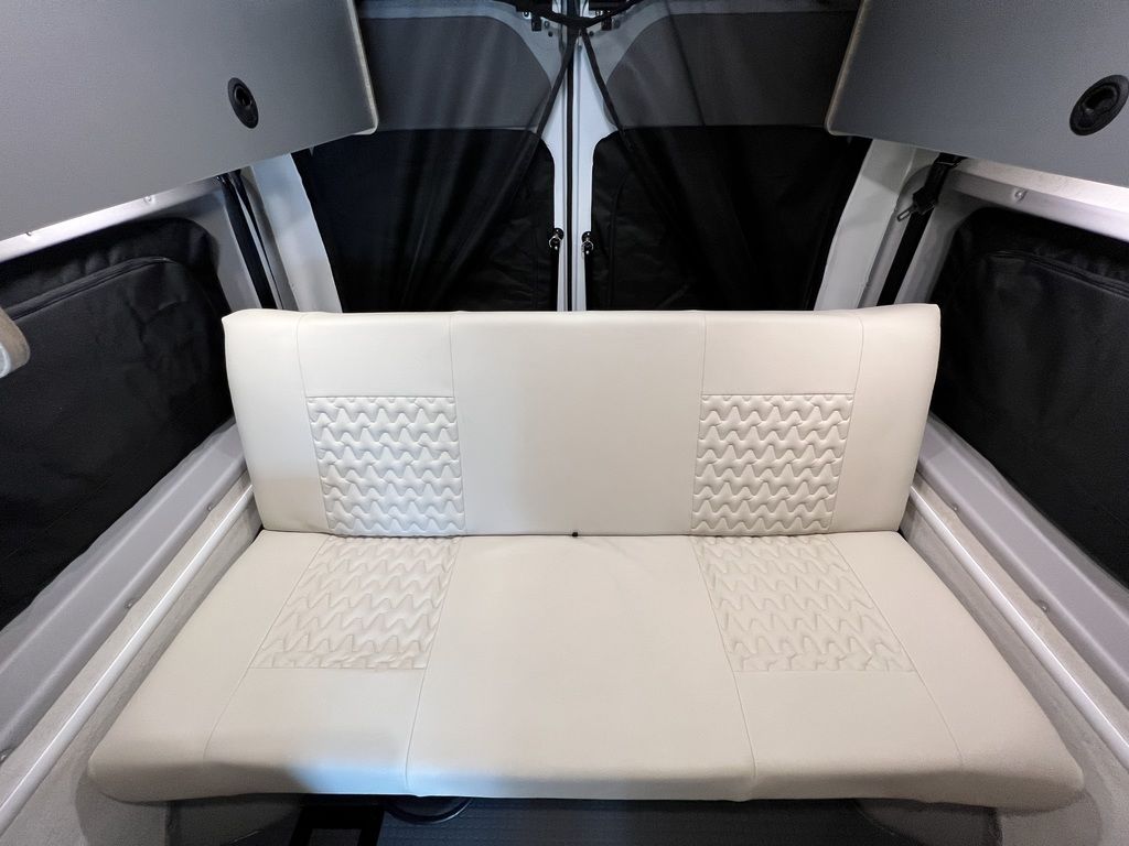 Inside an **rv rental**: light-colored bench seat with quilted cushions & storage bags. Cozy, compact camper interior.. Winnebago Solis 2021