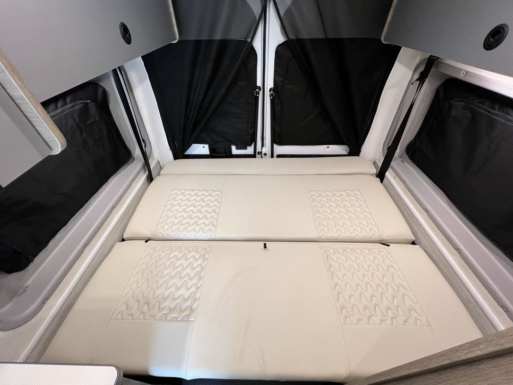 RV rental interior with a comfortable, cream-colored bed for two, complete with dark privacy window coverings.. Winnebago Solis 2021
