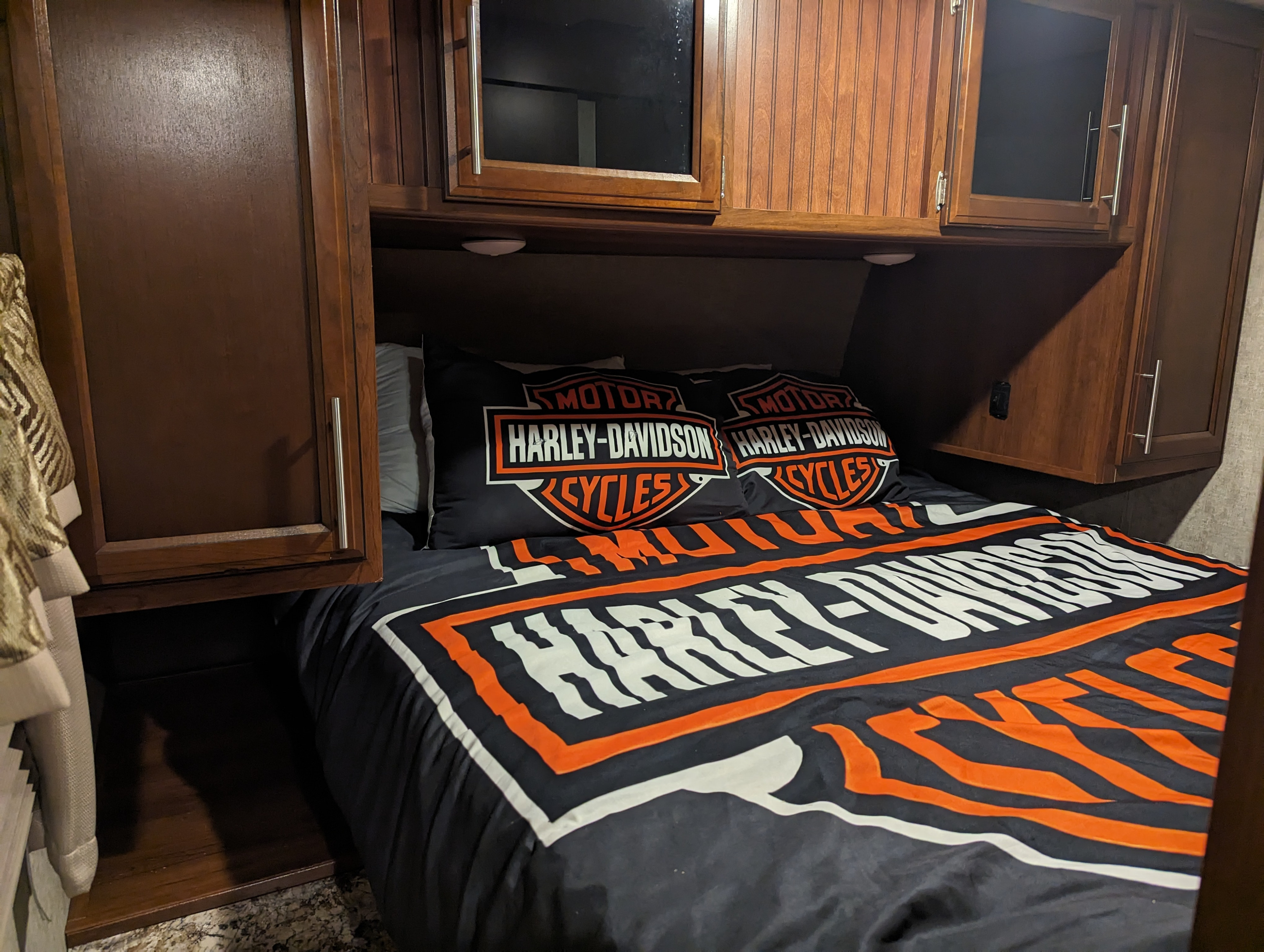 This RV rental bedroom features a comfy bed with bold Harley-Davidson bedding, tucked beneath wooden cabinetry.. Prime Time 2910 2017