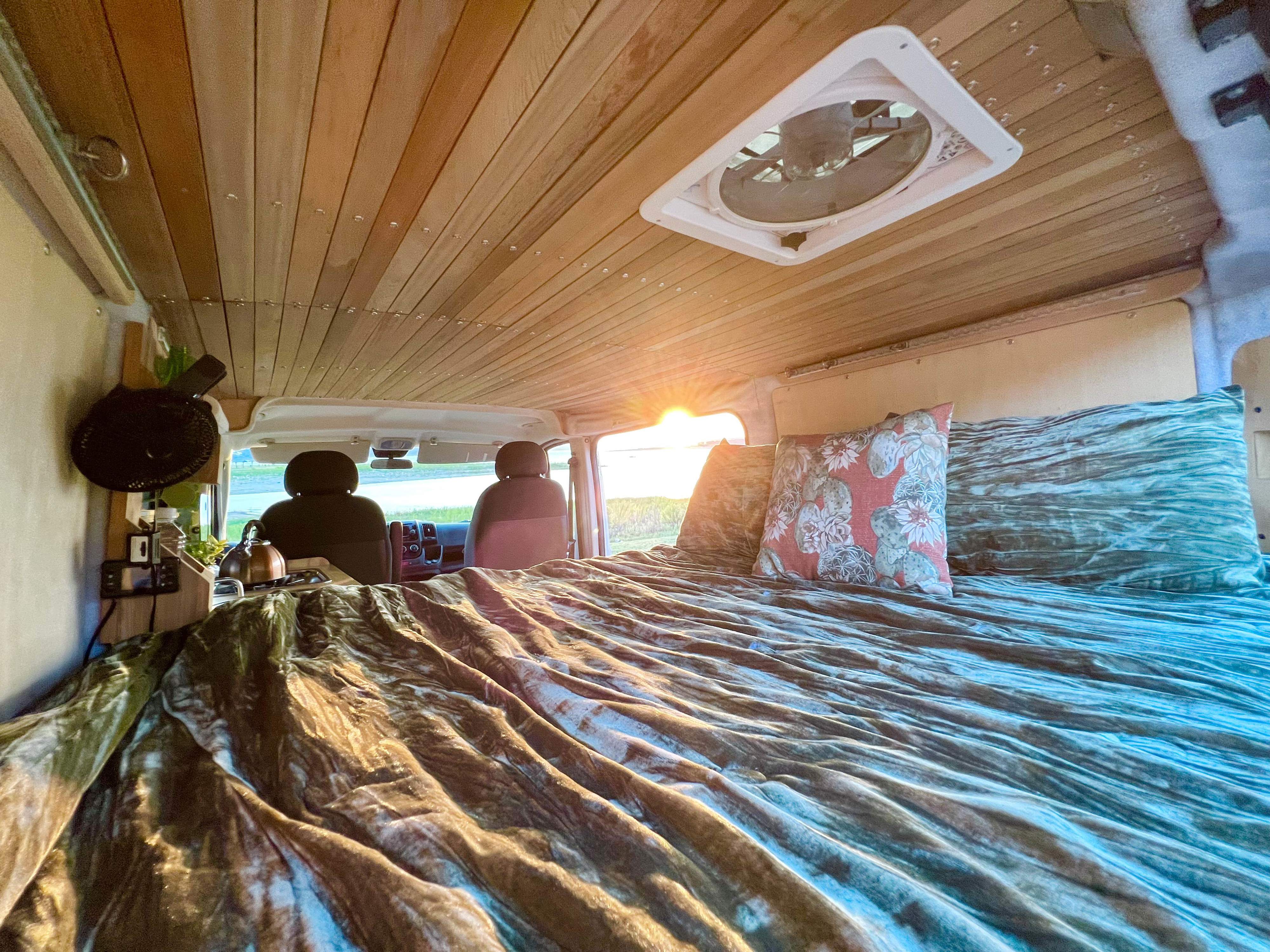 **RV rental** camper van interior: warm wooden ceiling, inviting bed, and sunset glow from the windshield.. Dodge RAM Promaster 2017
