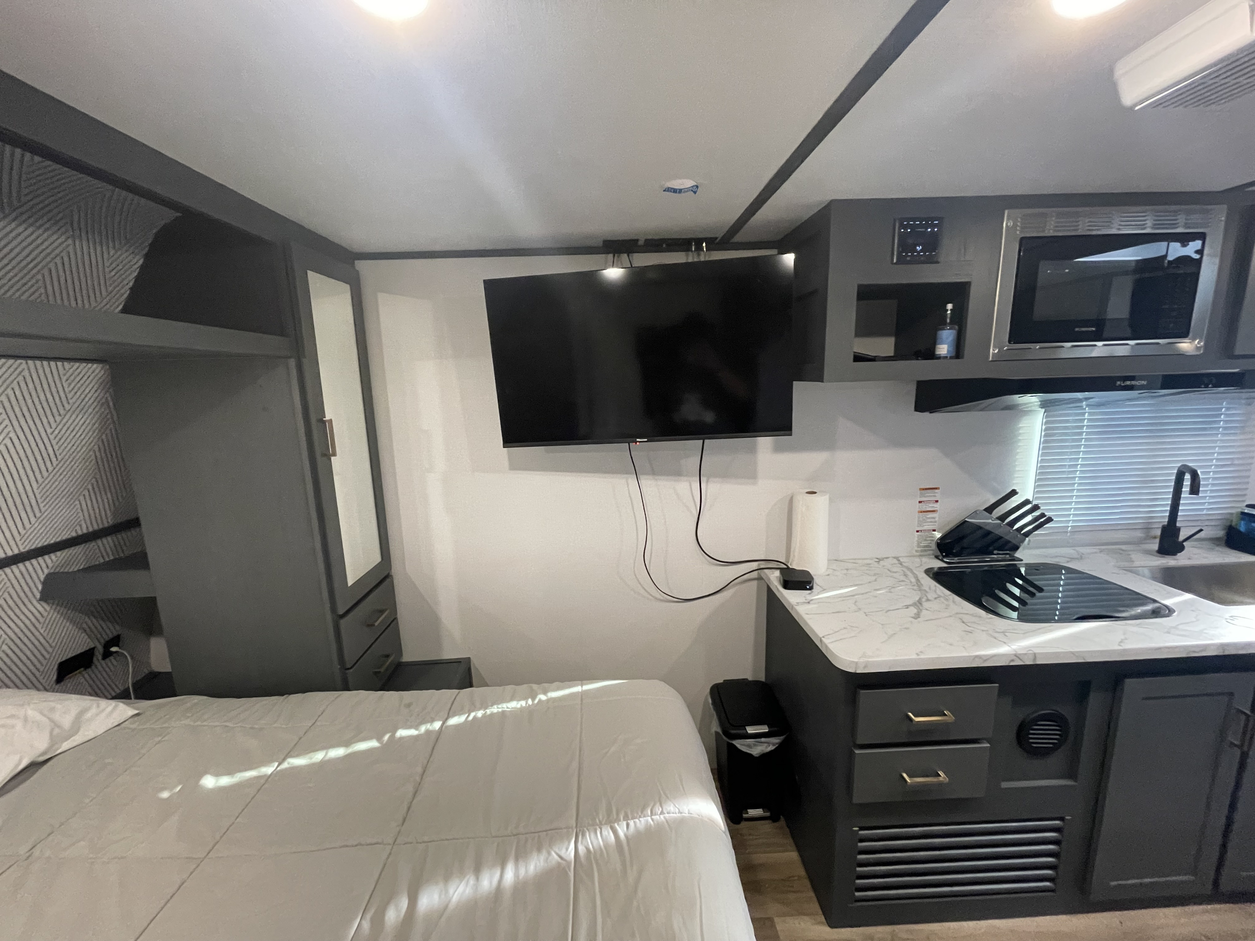 Compact RV rental interior featuring a modern kitchen with stove, microwave, and sink, alongside a comfortable bed.. Keystone RV Bullet Crossfire 2022