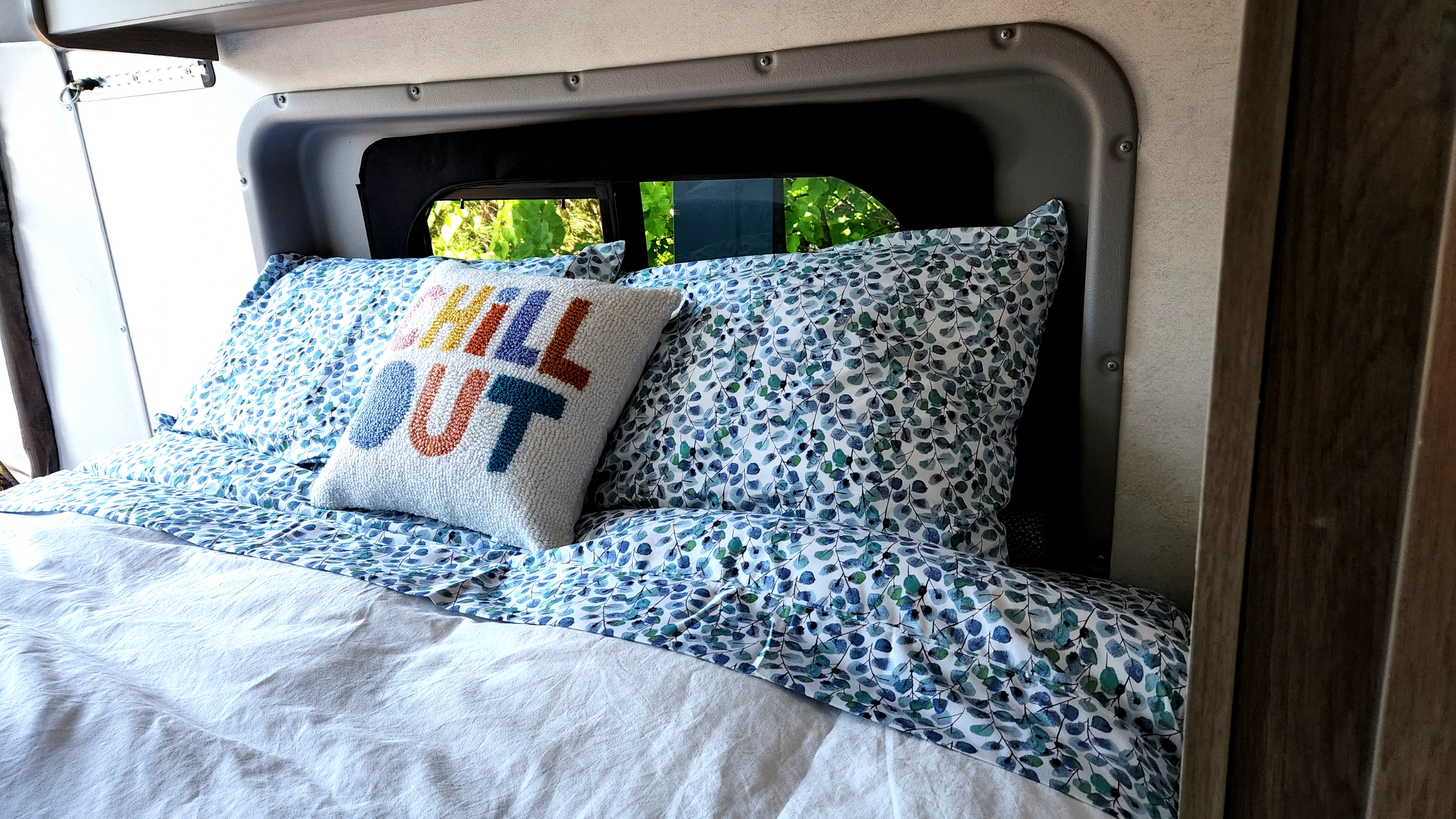 Inside a comfy RV rental: patterned bedding, "CHILL OUT" pillow, and window view. Great for road trips!. Winnebago Solis 2021