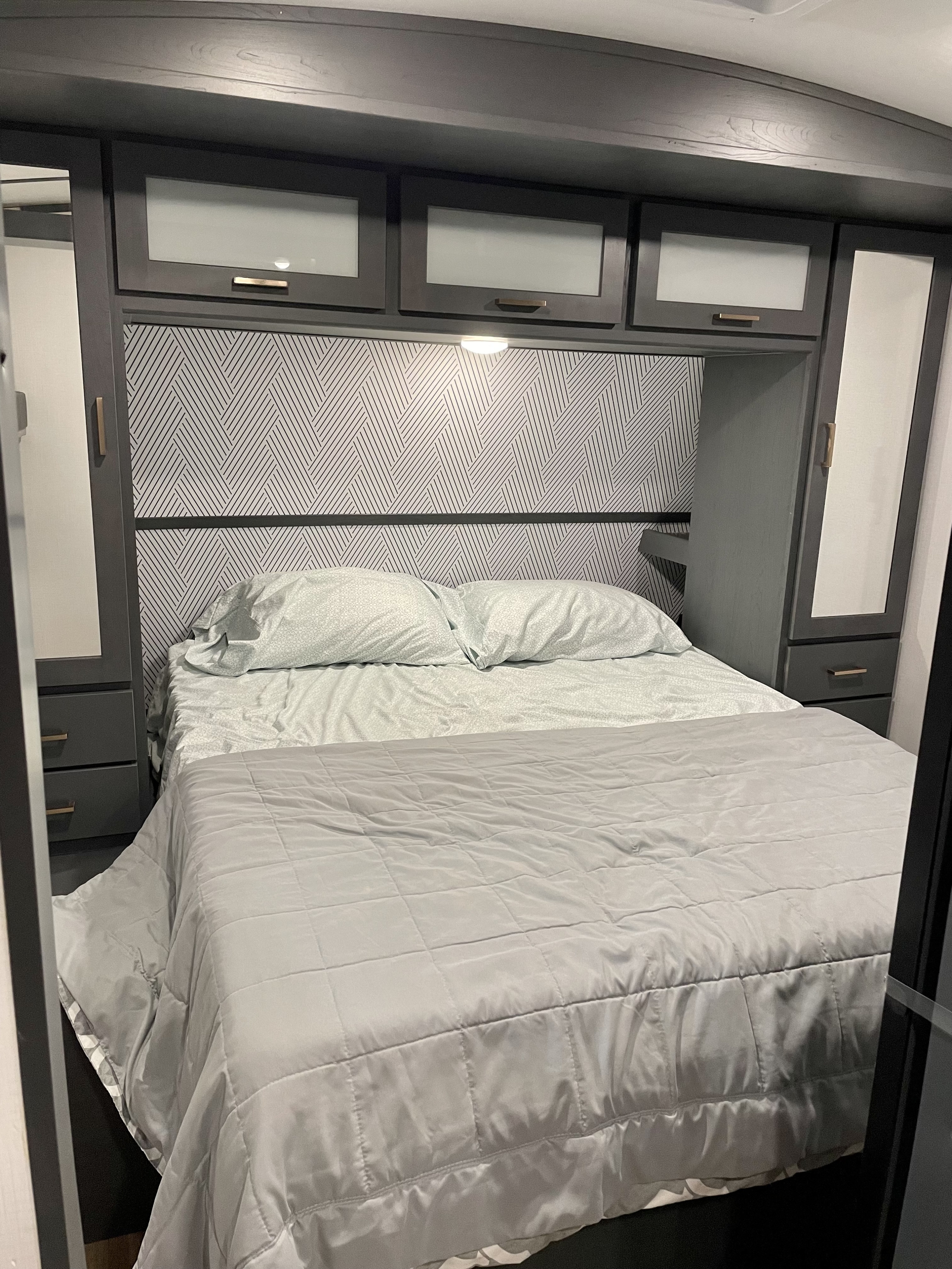 Modern gray RV rental bedroom interior with patterned headboard, ample storage cabinets, and comfy bed.. Keystone RV Bullet Ultra Lite 2022