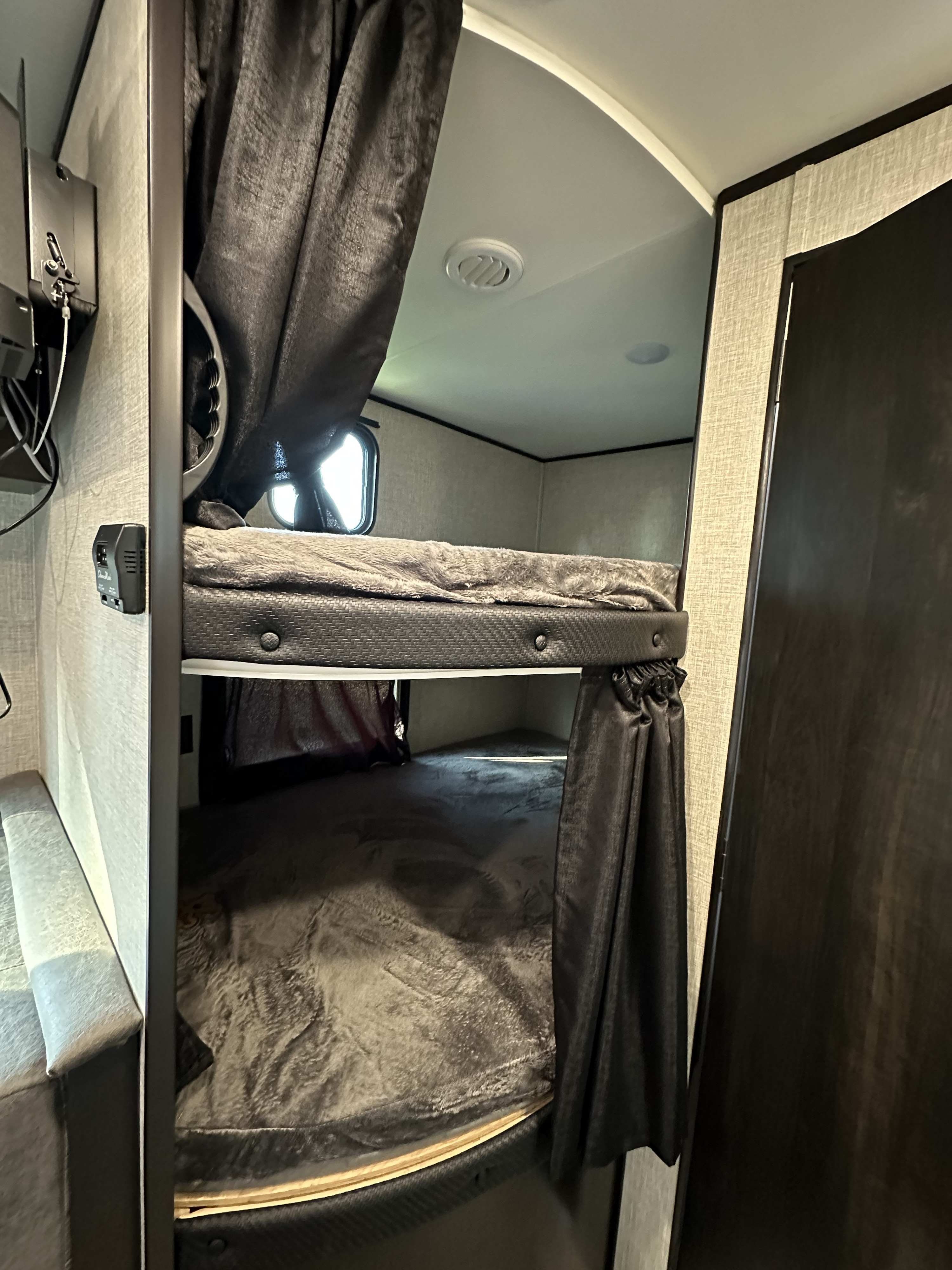 Cozy RV rental bunk beds with dark privacy curtains, plush grey bedding, and a small window for natural light. Ideal camper sleeping.. Jayco Jay Flight SLX 2022