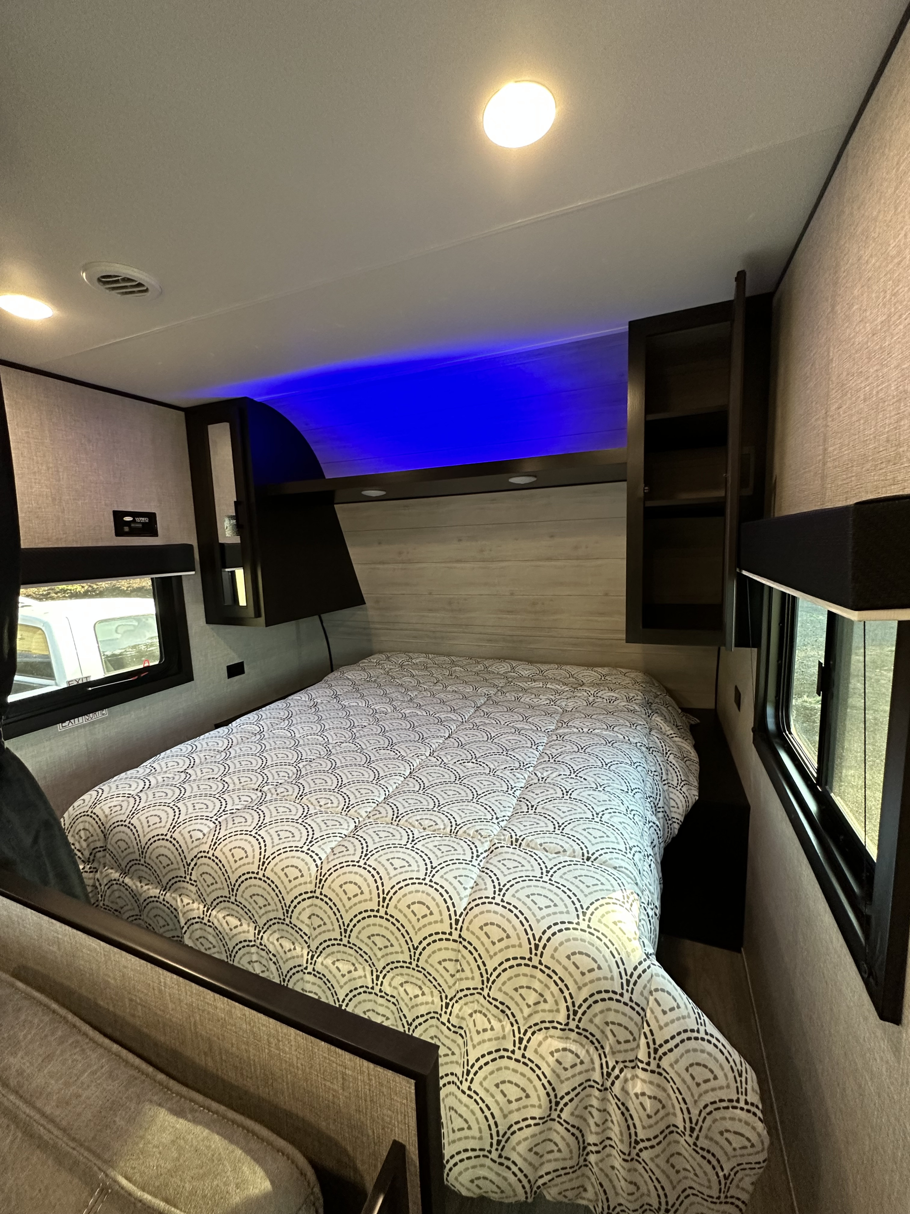 Cozy RV rental bedroom featuring a bed with patterned comforter, overhead storage, ambient lighting, and blue LED accents.. Jayco Jay Flight SLX 2022