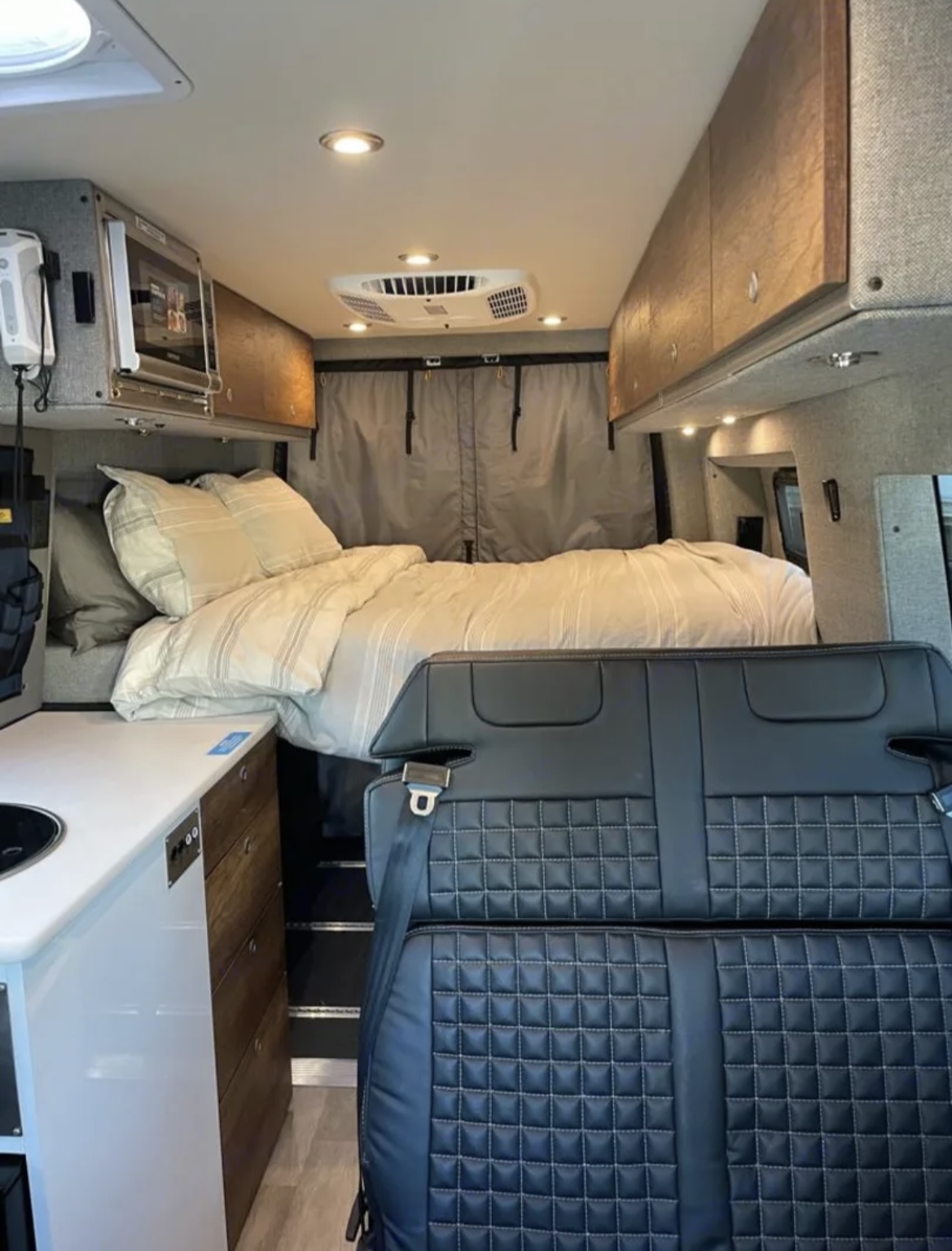 RV rental interior: cozy bed, mini kitchen, and quilted passenger seating in a well-appointed camper van.. Mercedes-Benz sprinter 2023