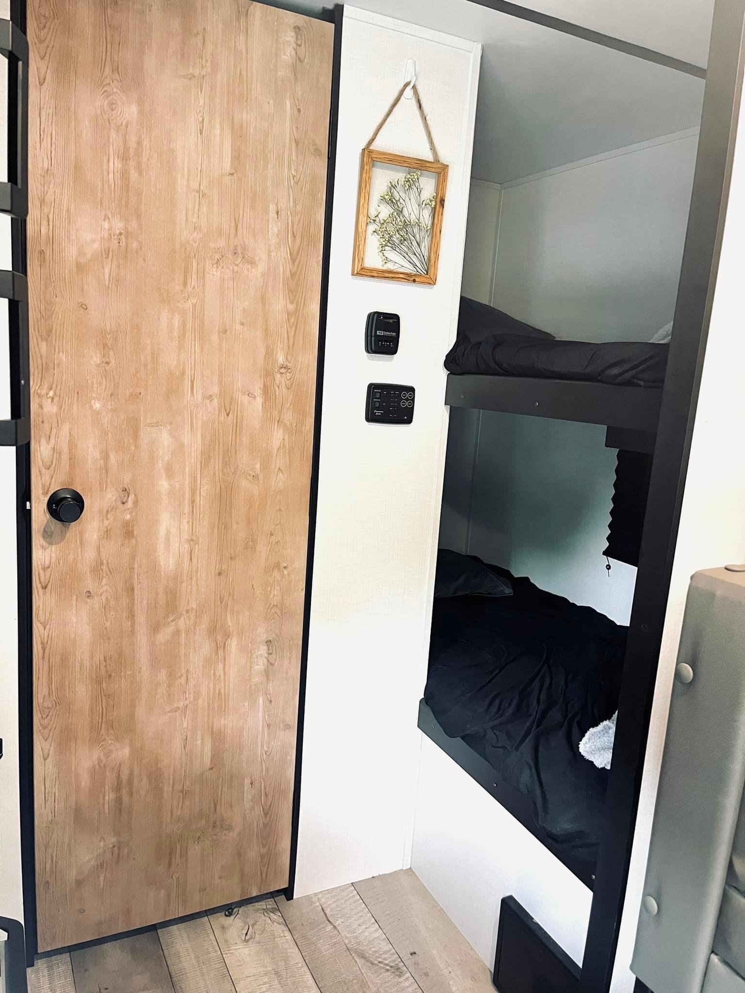 RV rental interior featuring stylish wood-grain door, bunk beds with black bedding, and control panels.. Keystone RV Springdale 2022