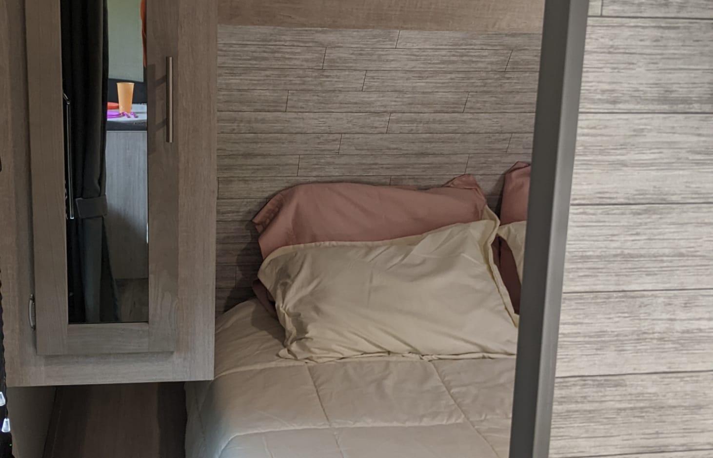 This cozy RV rental bedroom offers a comfortable bed with soft bedding, wood-paneled walls, and a convenient mirror.. Coachmen Other 2023