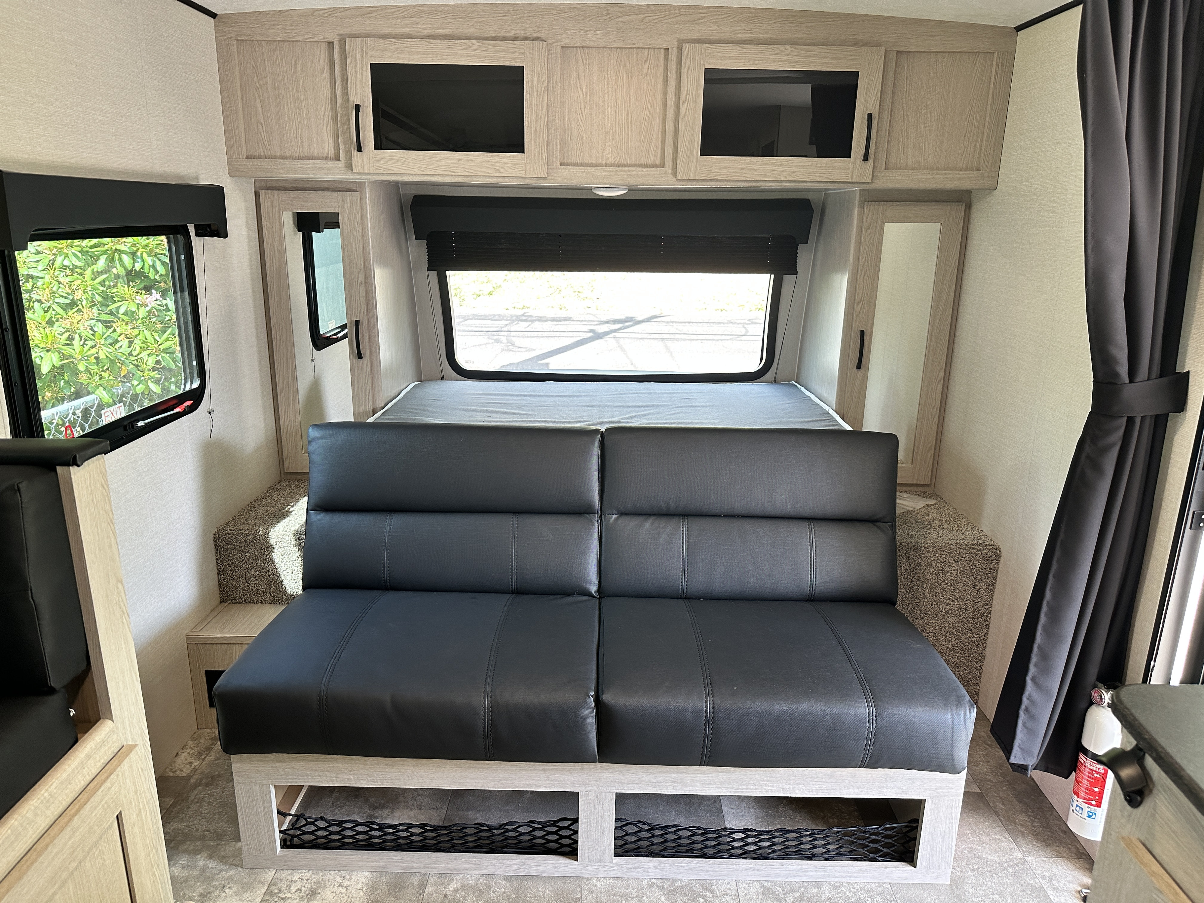 RV rental interior with a black leather-like sofa/bed, light wood cabinets, windows, and under-seat storage nets.. Coachmen Apex Nano 2022
