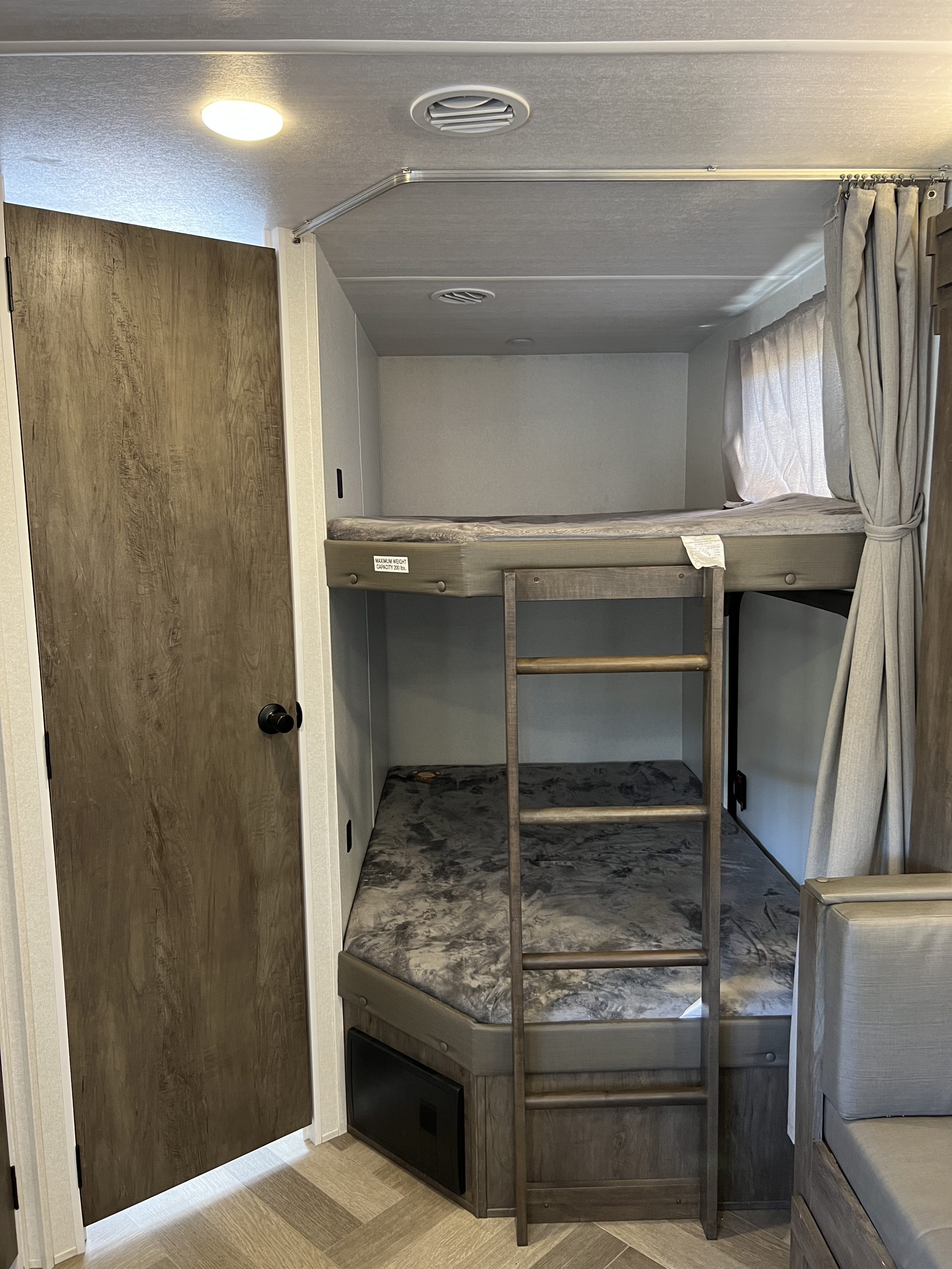 An RV rental's bunk bed setup, featuring a ladder, comfortable mattresses, and overhead ventilation.. Forest River Wildwood 2021