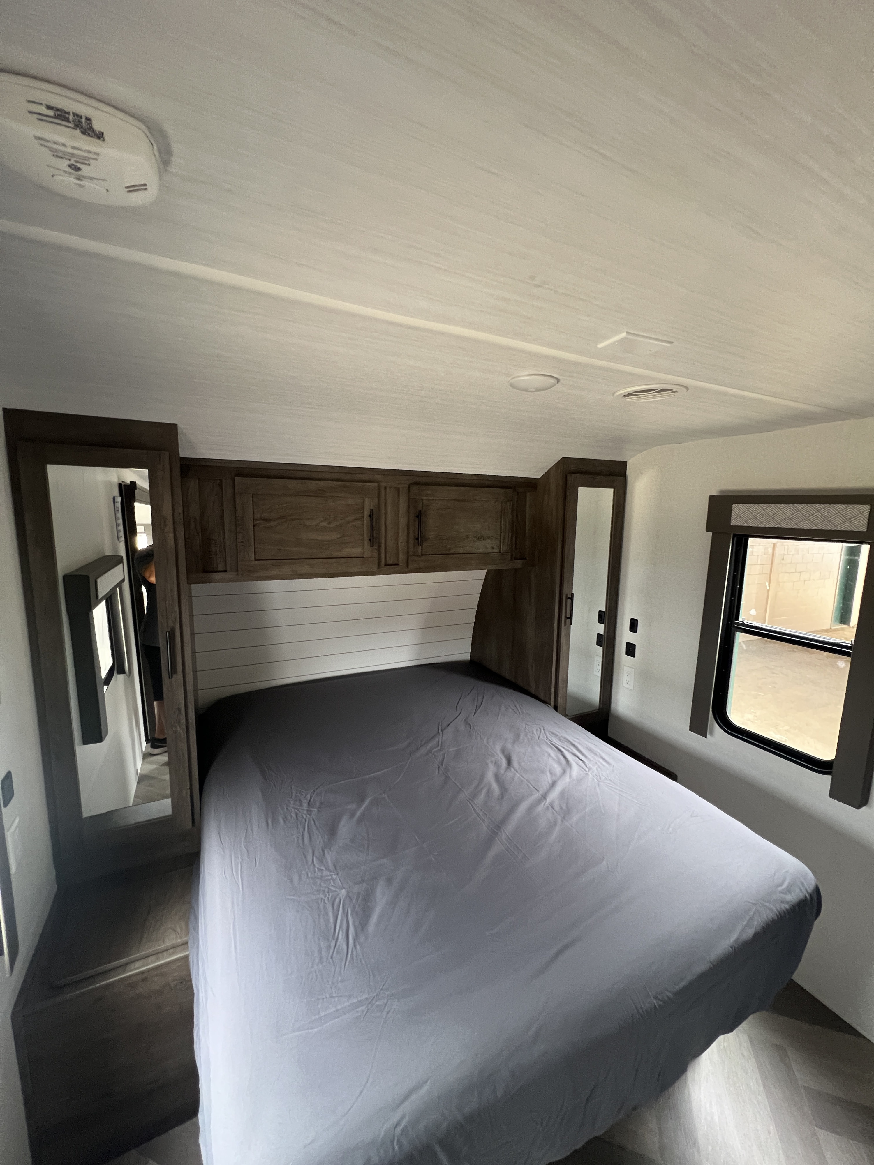 This RV rental bedroom features a gray bed, wooden cabinets, mirrors, and ceiling vents, offering a comfortable space.. Forest River Wildwood 2021