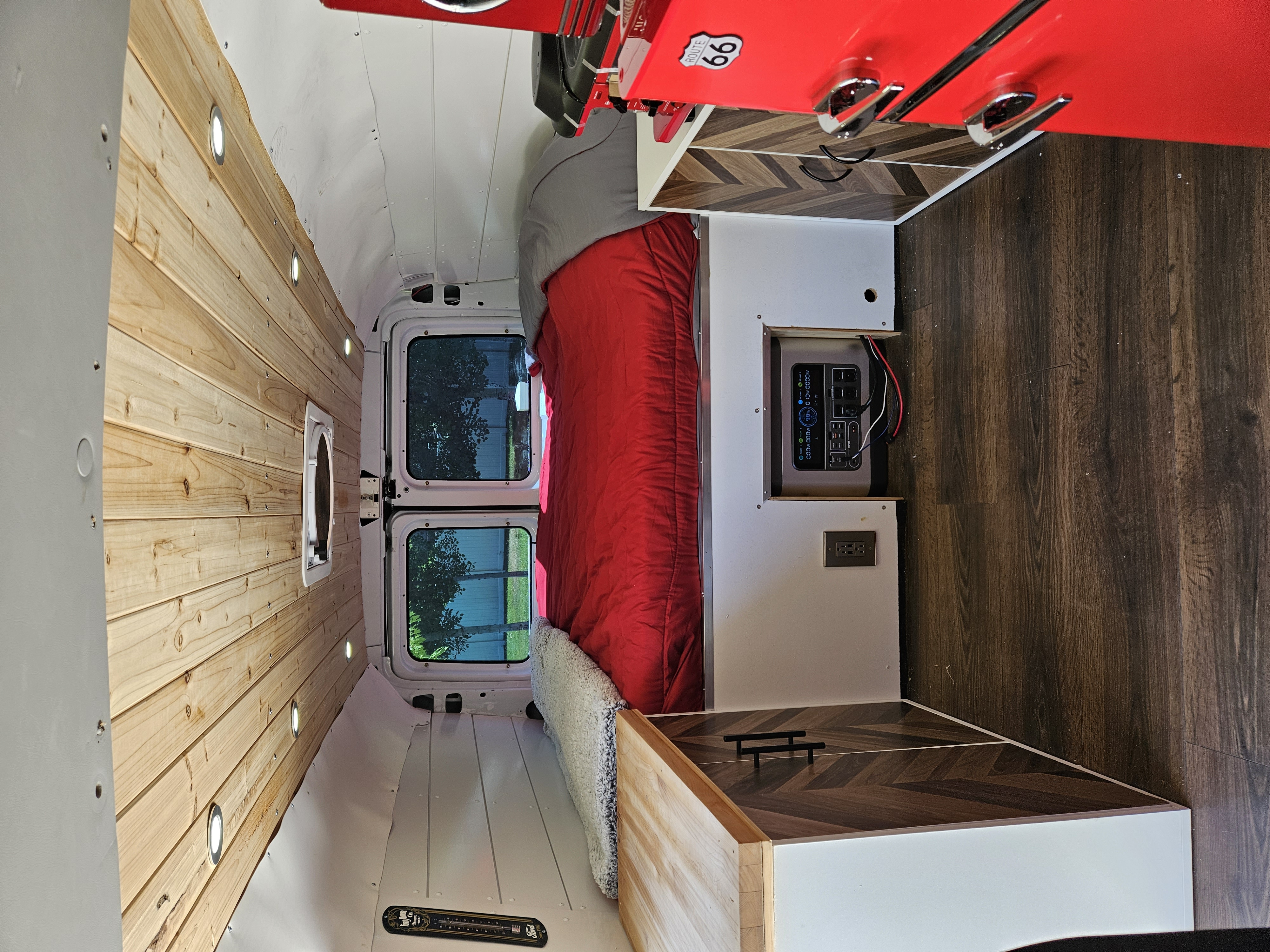 Inside a spacious RV rental camper van: wood walls, bed, kitchen area with red cabinets, and power station.. Ford Econolline 250s 2005