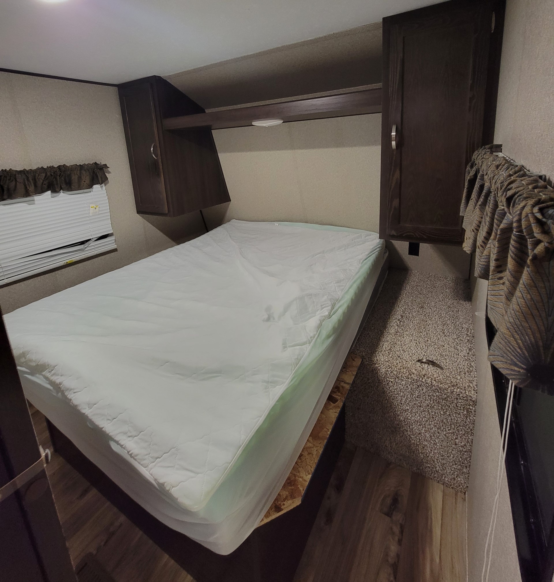Cozy RV rental bedroom with a comfortable bed, overhead cabinets, and window blinds, ideal for travel.. Keystone Summerland 2018