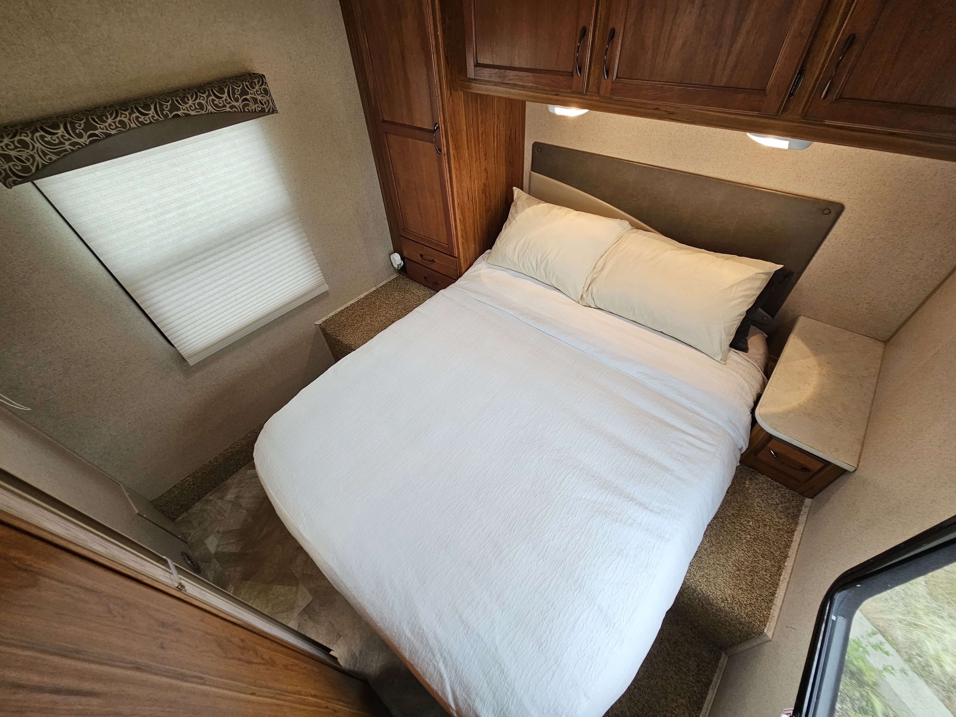Inside an rv rental, this cozy bedroom features a bed, wooden storage cabinets, window blinds, and overhead lighting.. Jayco Redhawk 2015