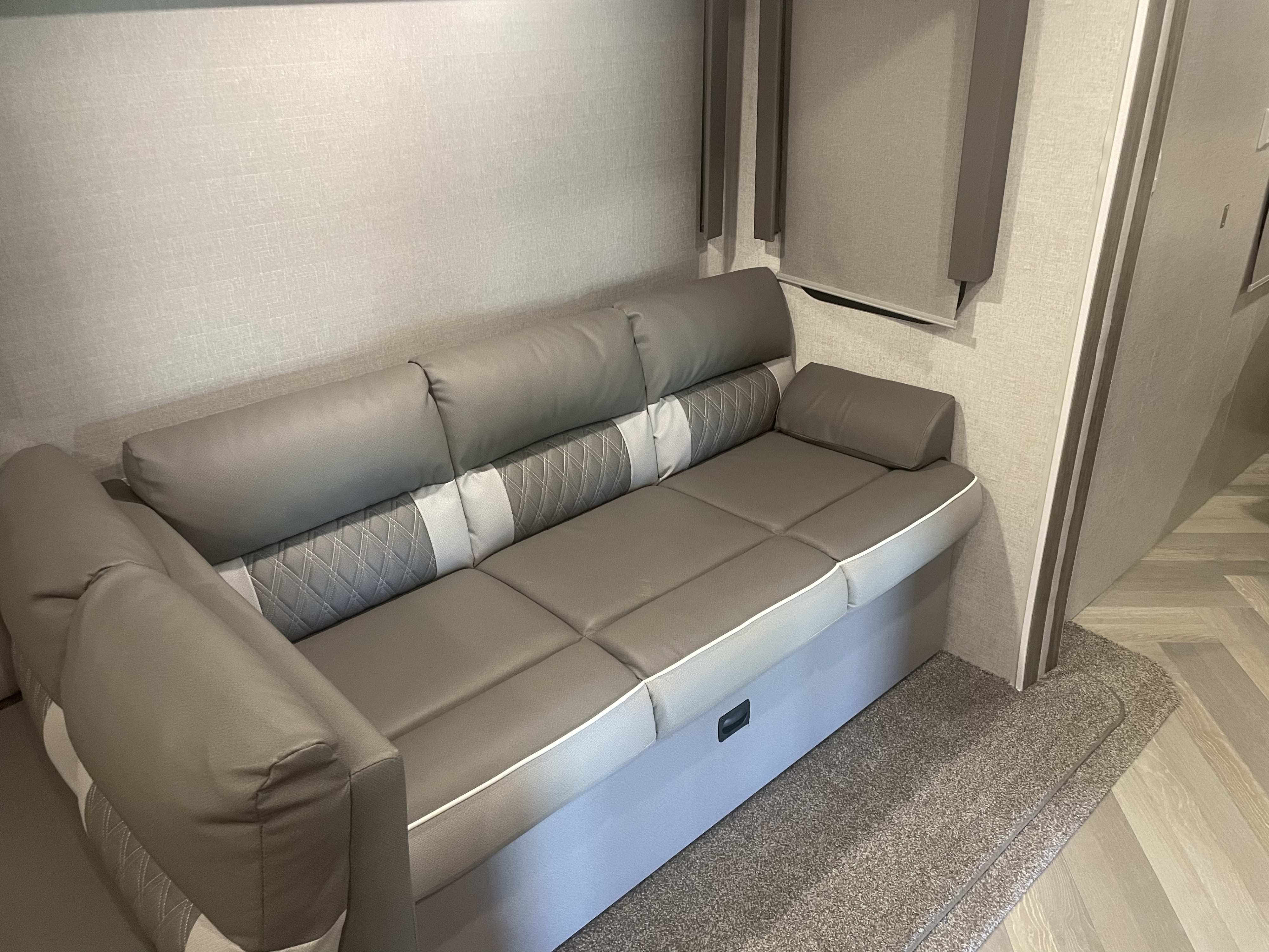 Interior view of an RV rental, showing a comfortable grey sofa with patterned accents, window shade, and textured walls.. Forest River Salem 2021