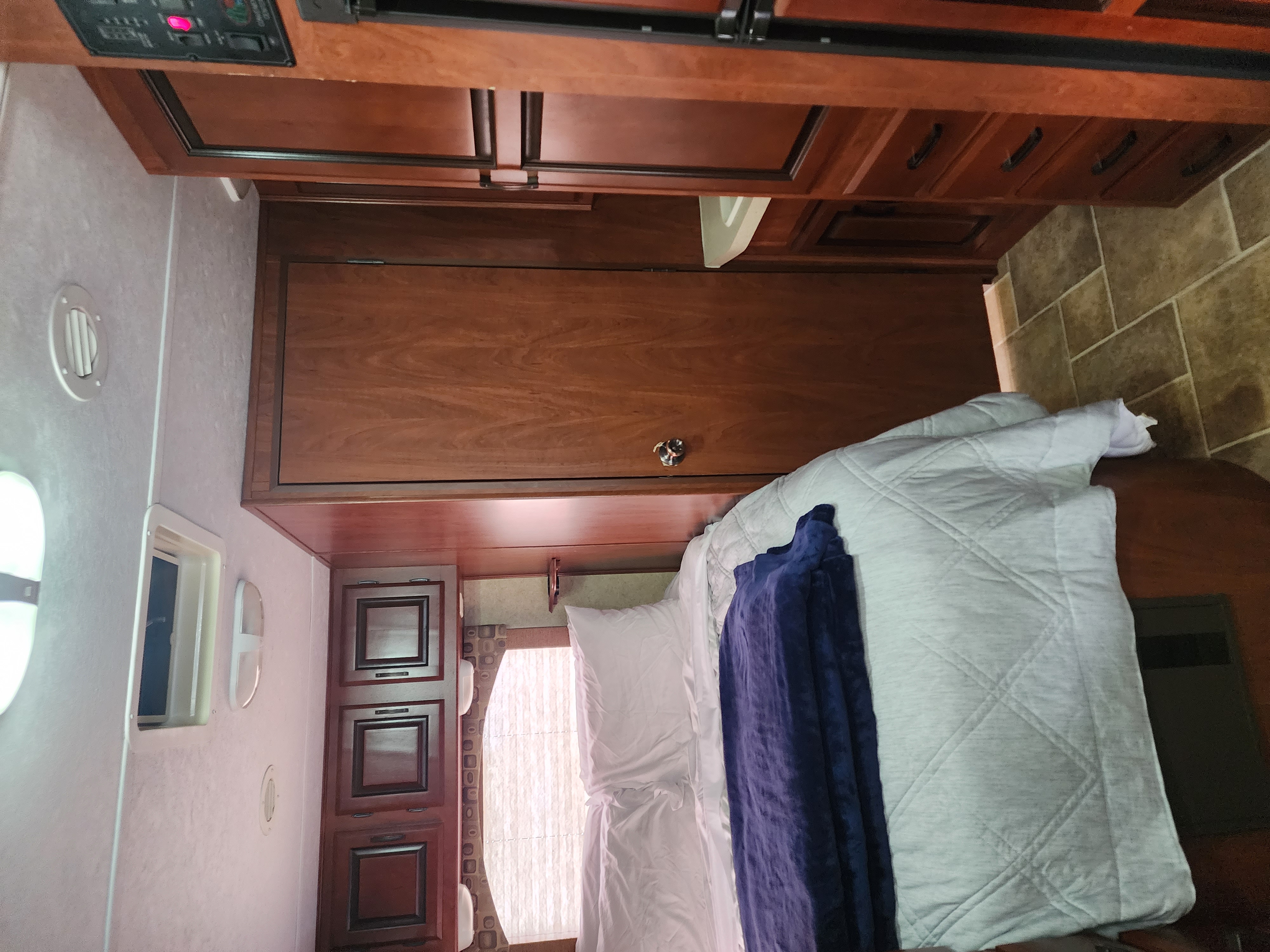 Cozy interior of an RV rental bedroom, showcasing wood cabinetry, a comfortable bed with white and blue bedding, and control panel for utilities.. Forest River Sunseeker 2012