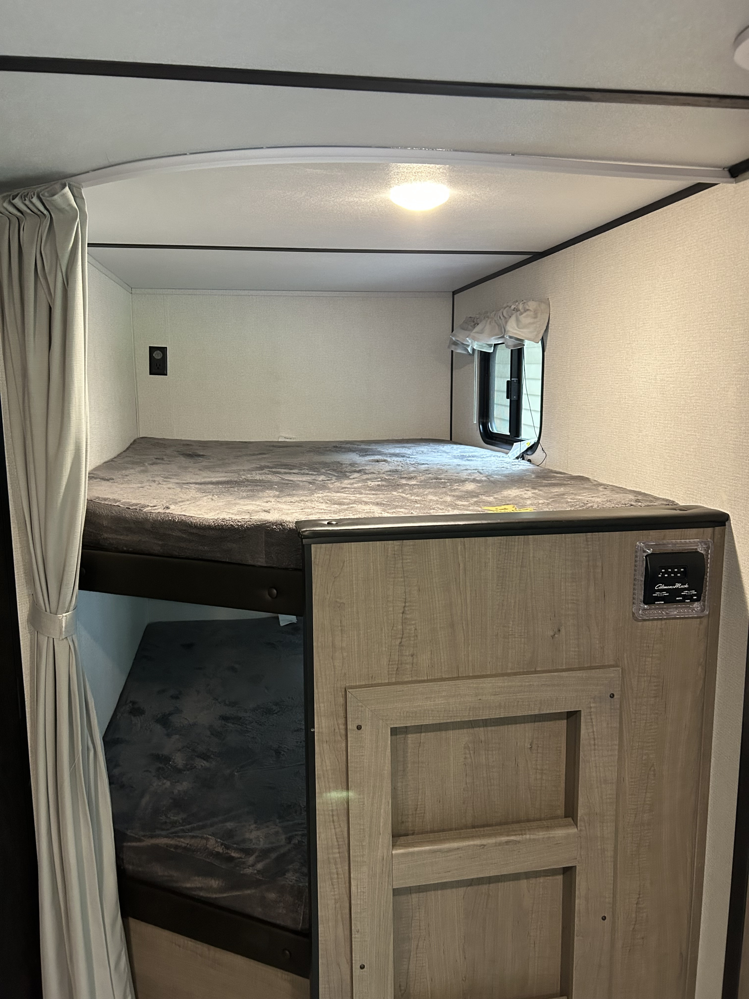 Cozy RV rental bunk beds with curtains, window, and thermostat, providing a comfortable and compact sleeping space.. Keystone Hideout 2023