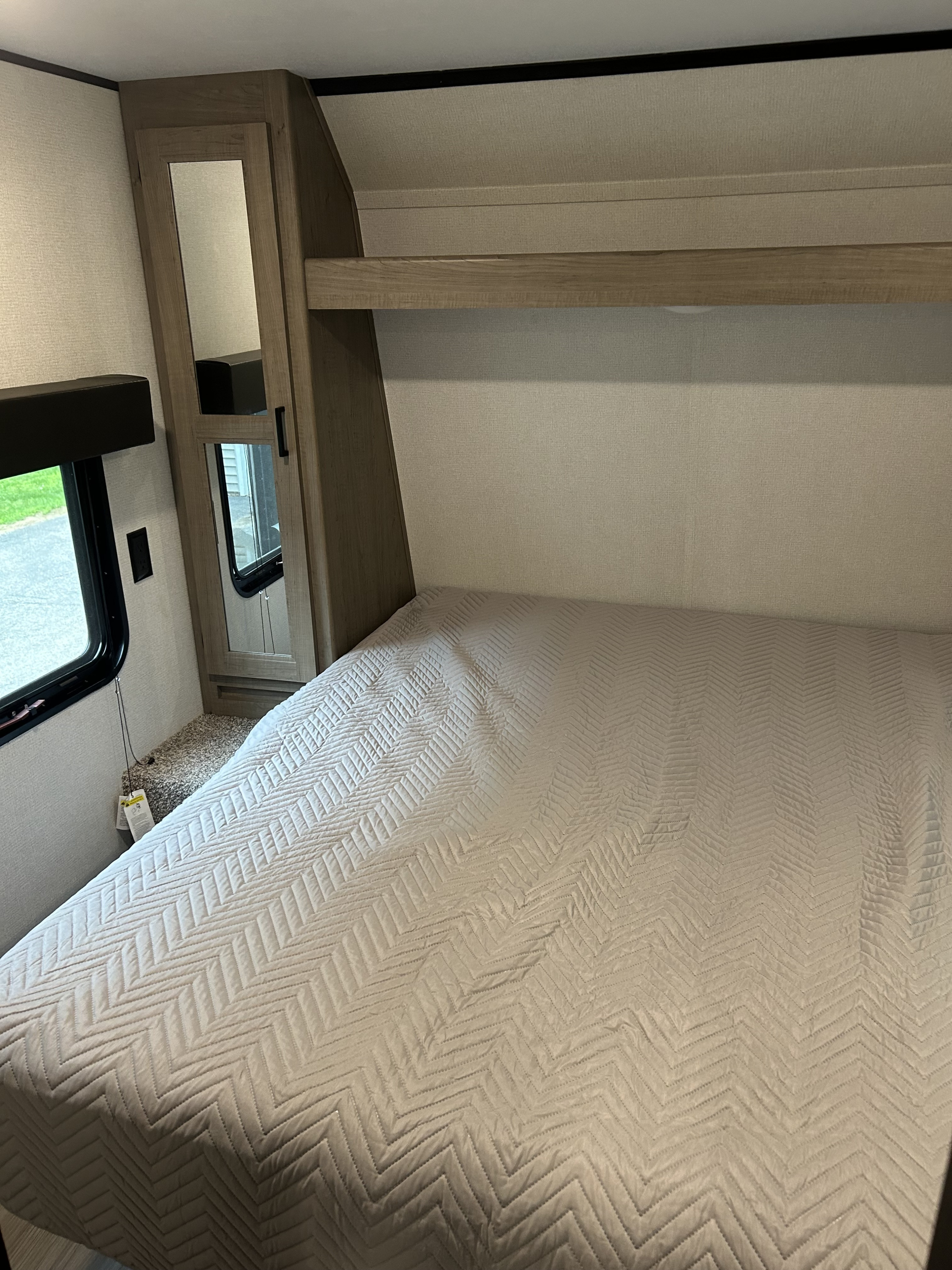 Cozy RV rental bedroom with a chevron-quilted bed, window, overhead shelf, and mirrored storage cabinet.. Keystone Hideout 2023