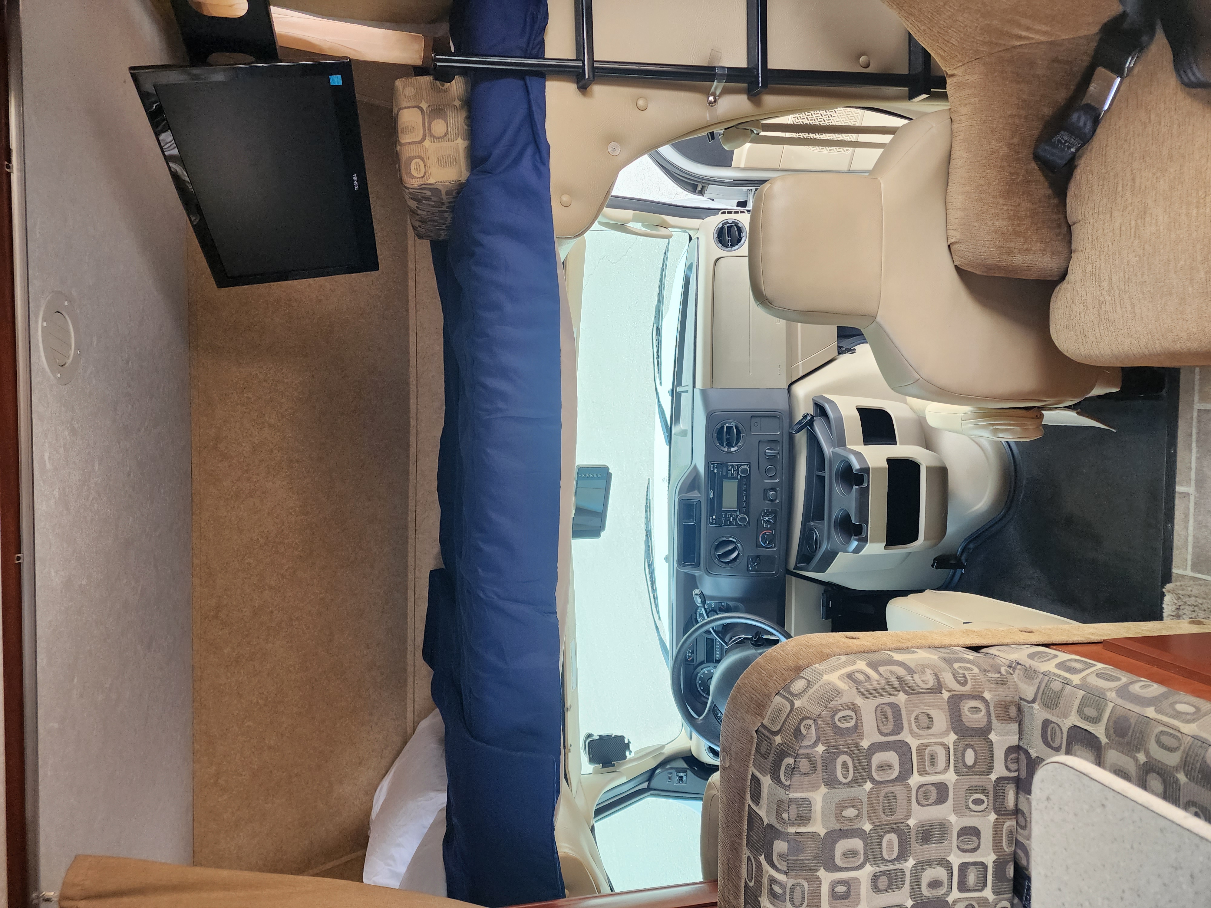 Inside an RV rental: overhead bunk with blue bedding, Toshiba TV, and front cockpit area with tan seats.. Forest River Sunseeker 2012