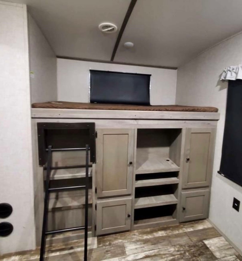 Inside an RV rental, a bunk bed sits above a multi-section storage unit with cabinets, shelves, and a metal access ladder.. Keystone RV Outback 2021