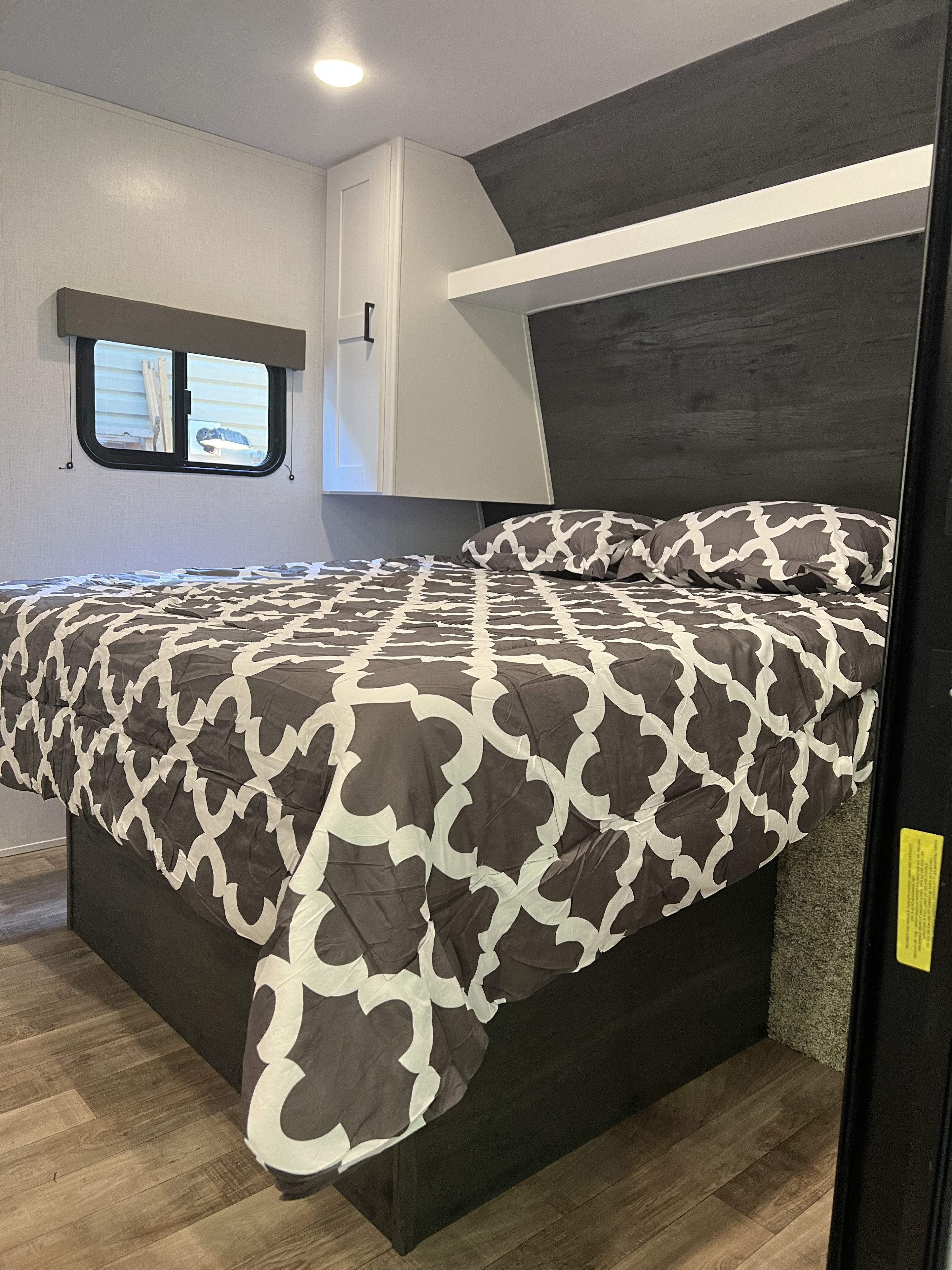 Cozy RV rental bedroom: Features a comfortable bed with grey and white patterned bedding, overhead cabinets, and a window view.. Keystone RV Hideout 2022