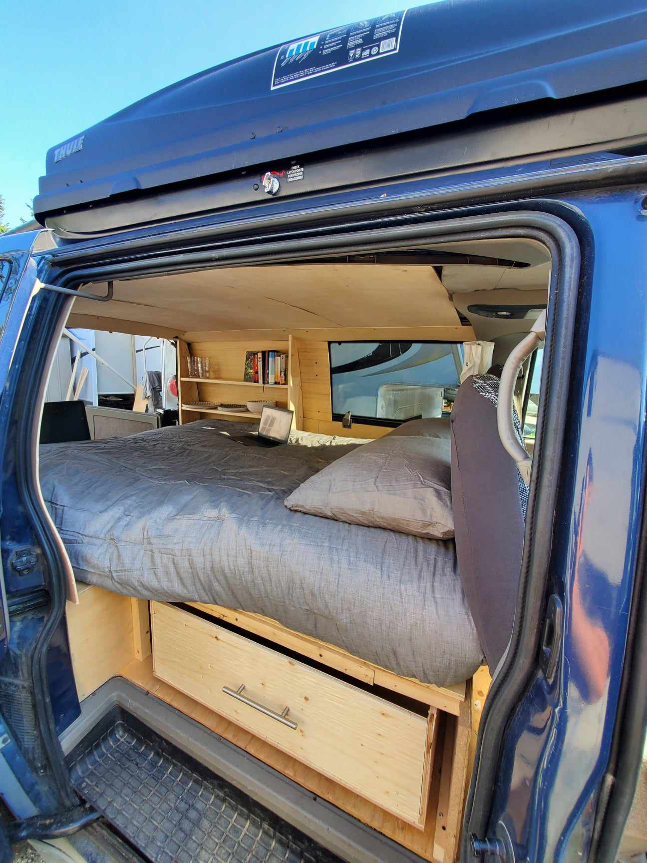 Inside a spacious RV rental: a blue camper van converted with a comfortable bed, wood storage, and built-in shelving.. Gmc Safari 1999