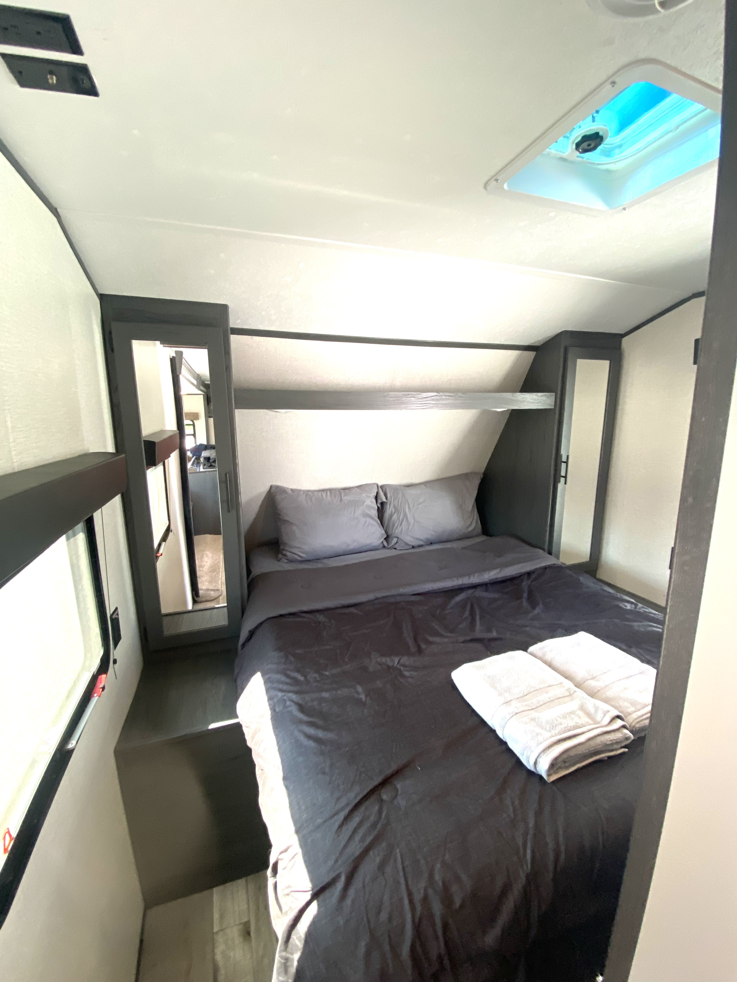 RV rental bedroom: Comfortable bed with dark linens, grey pillows, two towels, built-in storage, window, and mirrored door.. Aspen Trail Aspen Trail Trailer 2021