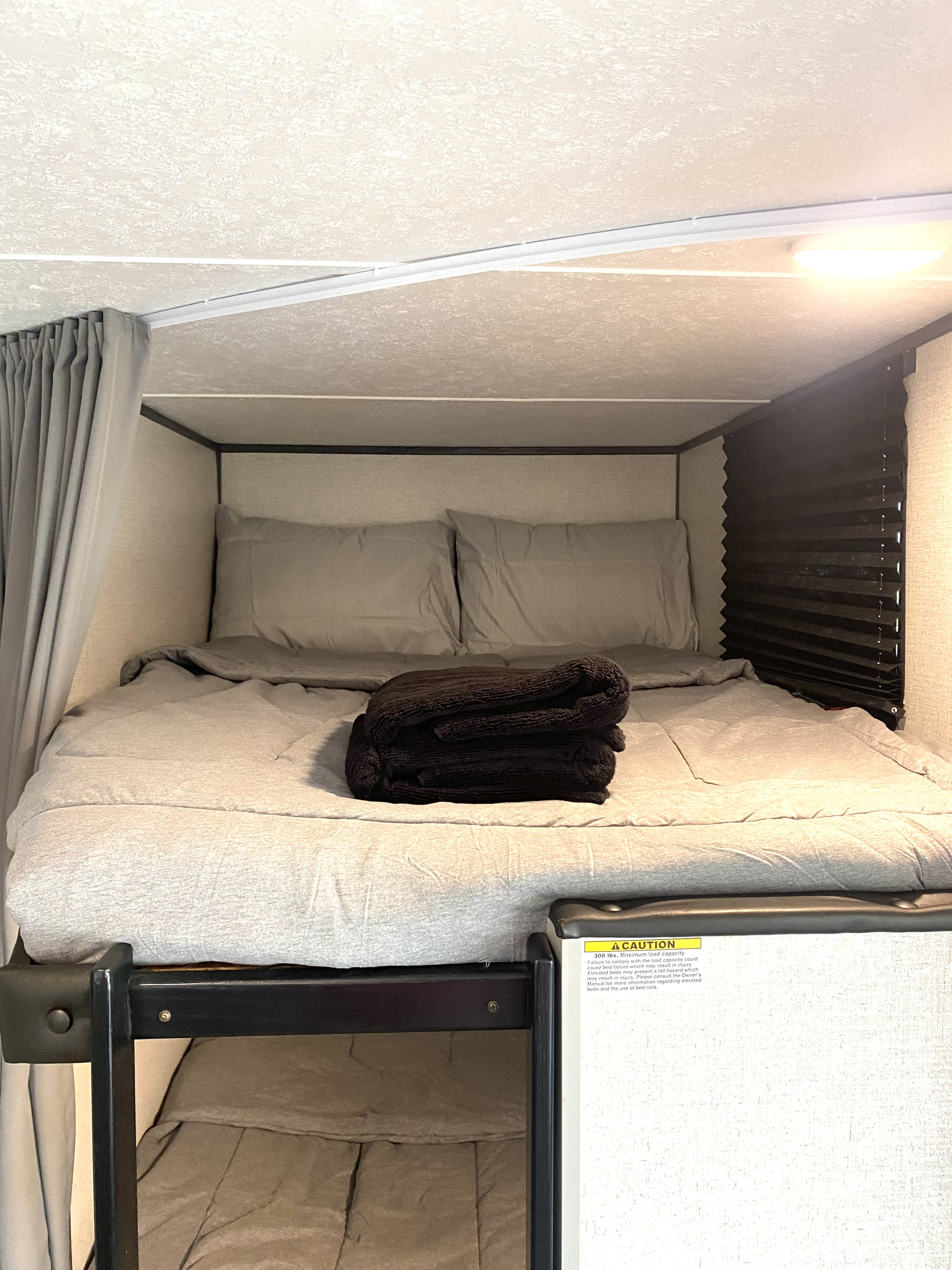 Comfortable RV rental bunk bed with grey linens and a dark blanket, ready for a cozy night's sleep in a compact interior.. Aspen Trail Aspen Trail Trailer 2021