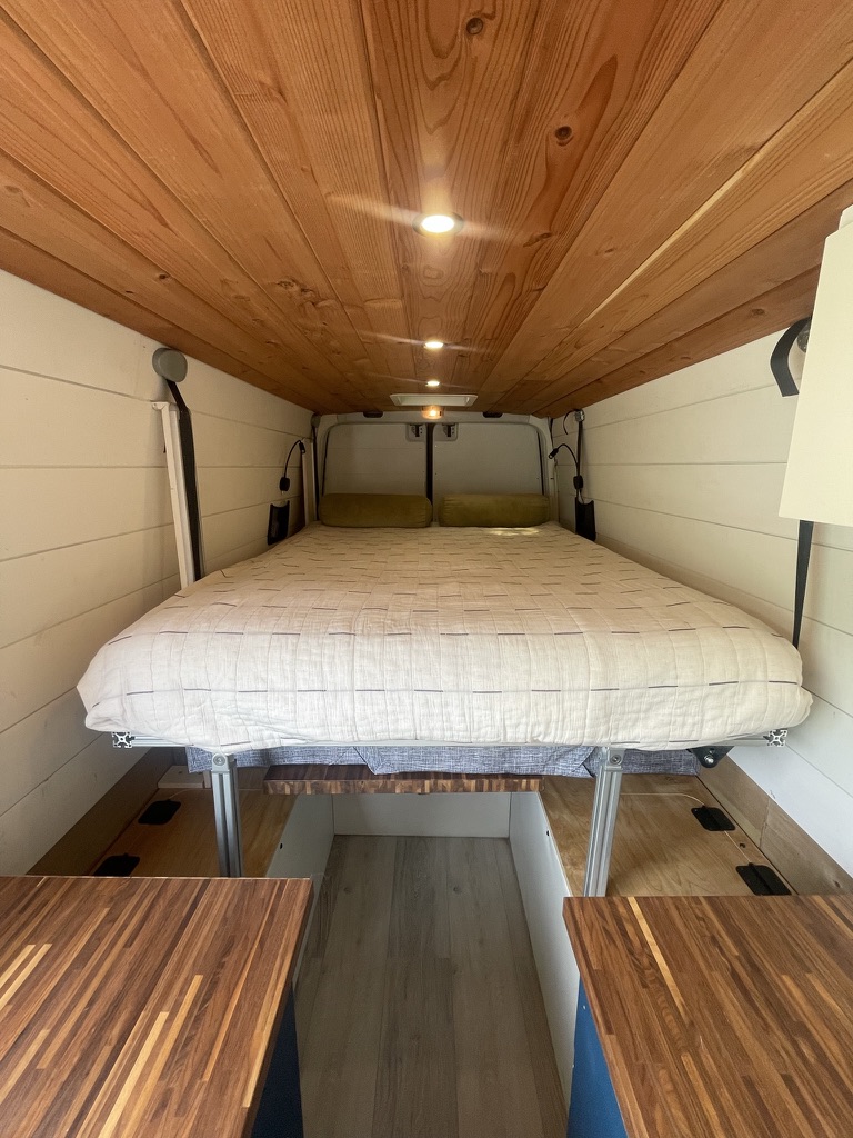 Cozy camper van interior for RV rental adventures. Features a raised bed, wood ceiling, and warm lighting.. Mercedes Sprinter 2010