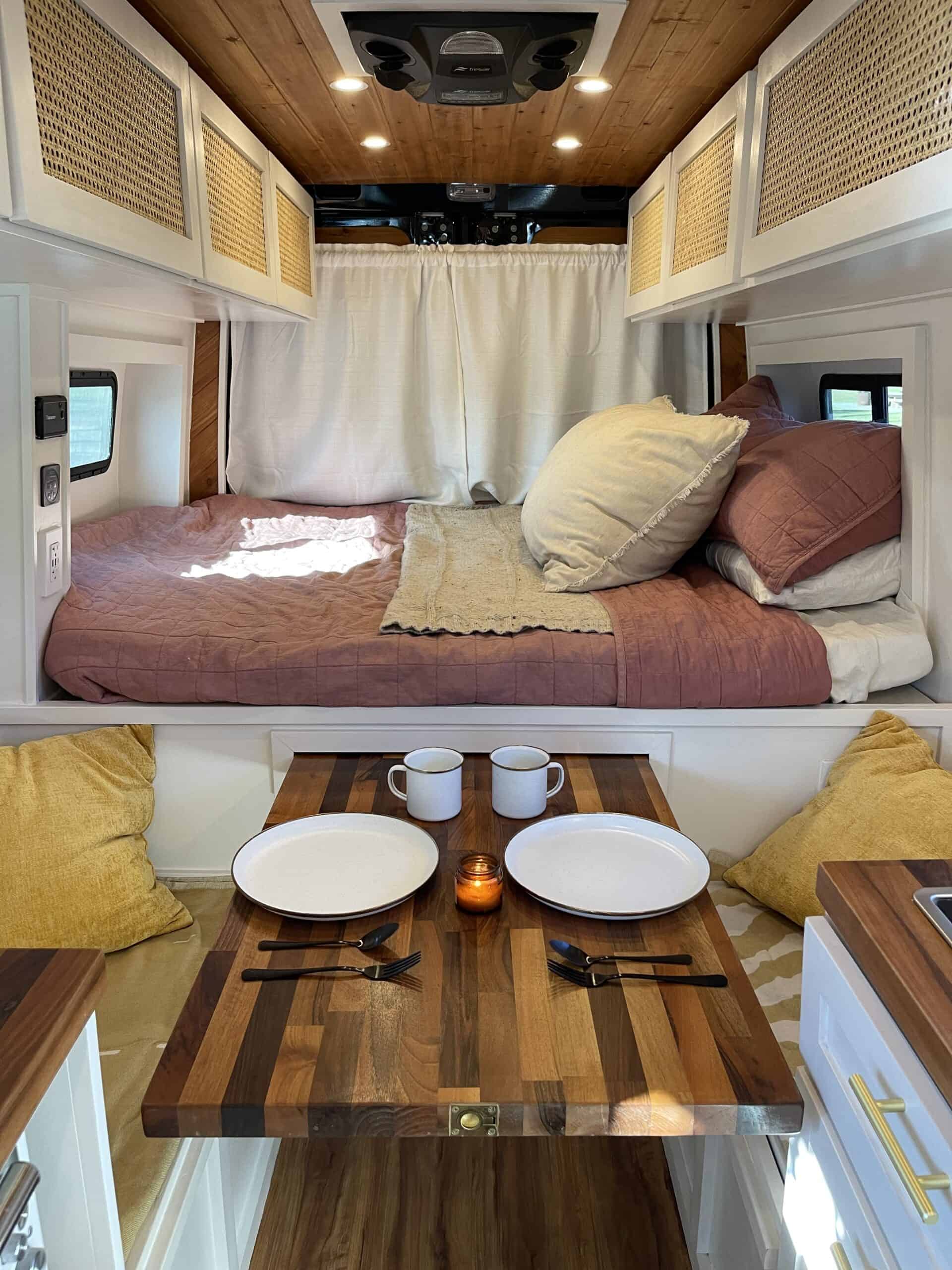 Beautiful RV rental interior: bed with pillows, wooden ceiling, rattan cabinets, and a cozy dining area set for two.. Mercedes-Benz Sprinter 2021