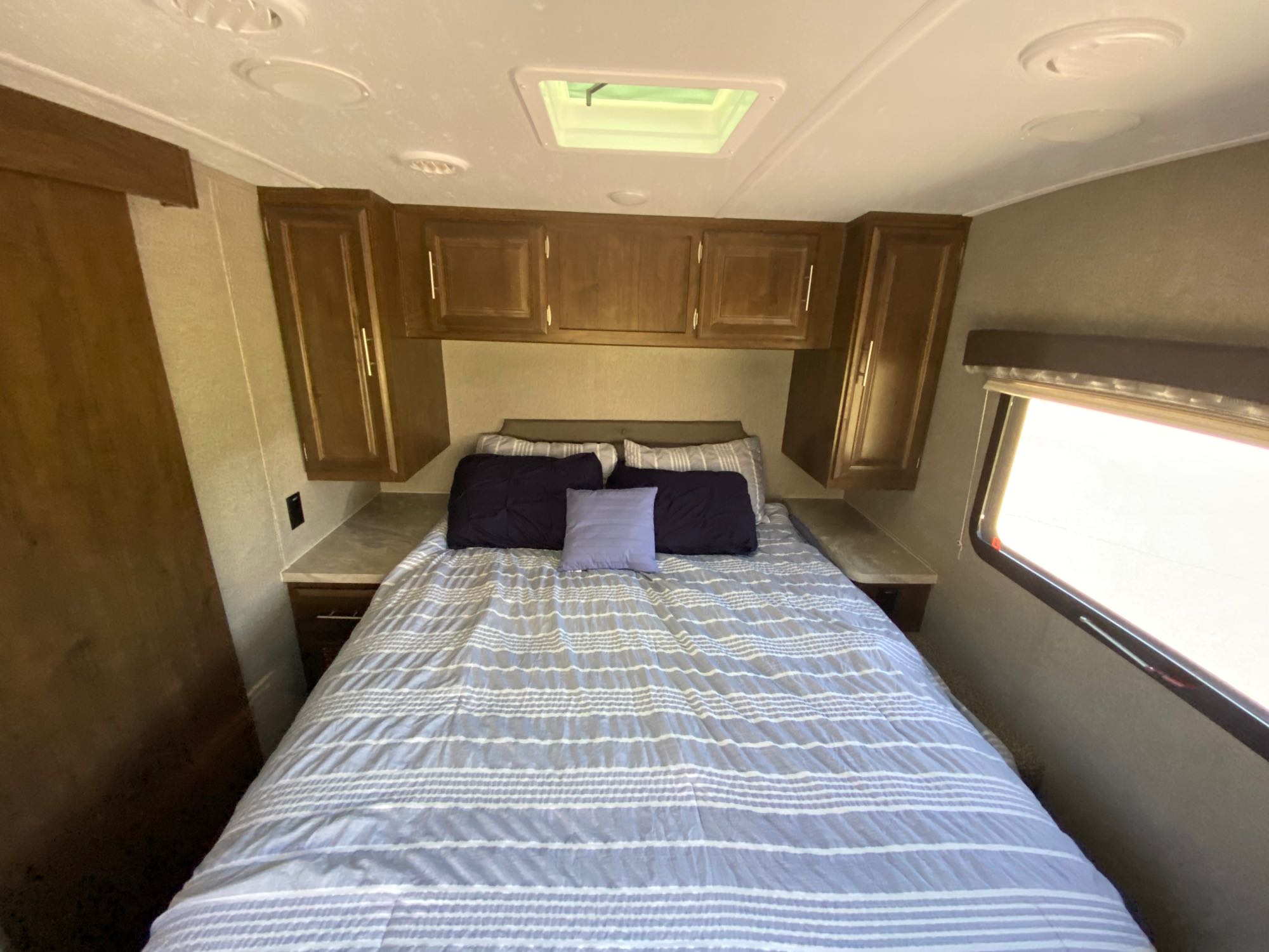 Comfortable RV rental bedroom interior with a striped bed, overhead cabinets, a skylight, and a window.. Forest River Rockwood Mini Lite 2506s 2021