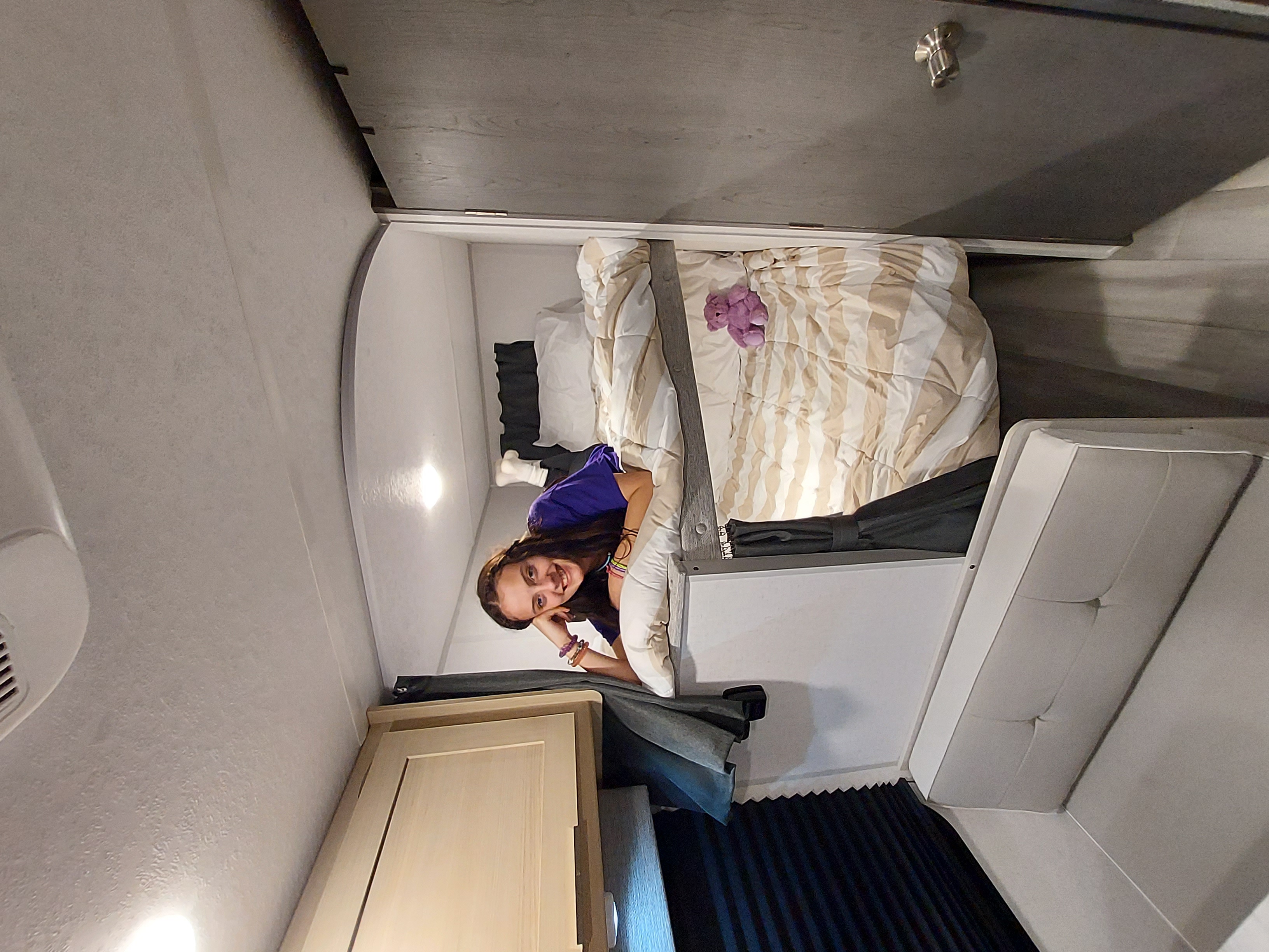 Enjoying a cozy RV rental bed: a young woman smiles surrounded by soft bedding and built-in comforts.. Forest River Salem FSX Platinum 2023