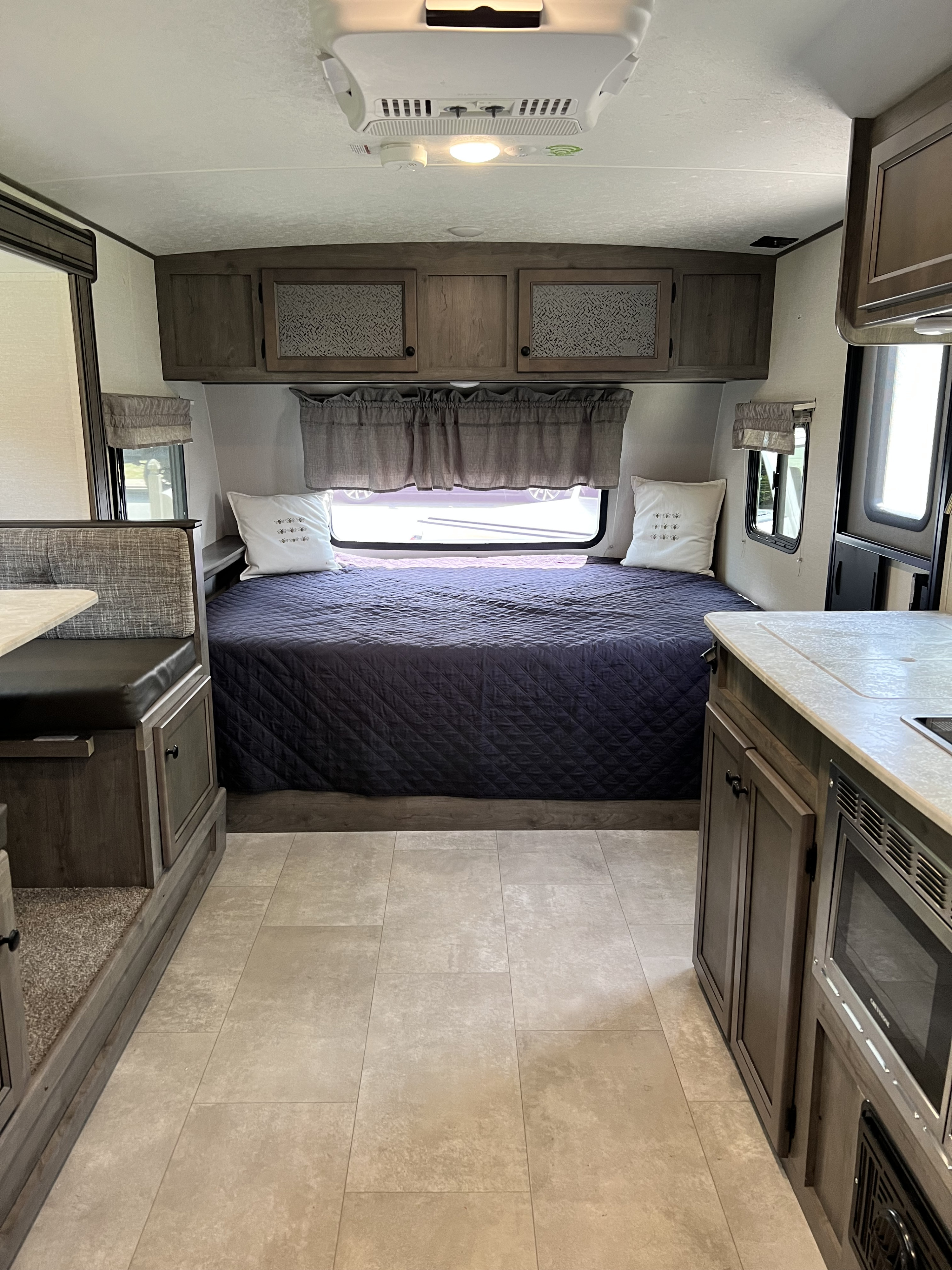 Modern RV rental interior with a cozy bed, dinette, and compact kitchen area. Ideal for comfortable travel.. Coachmen Apex Nano 2021