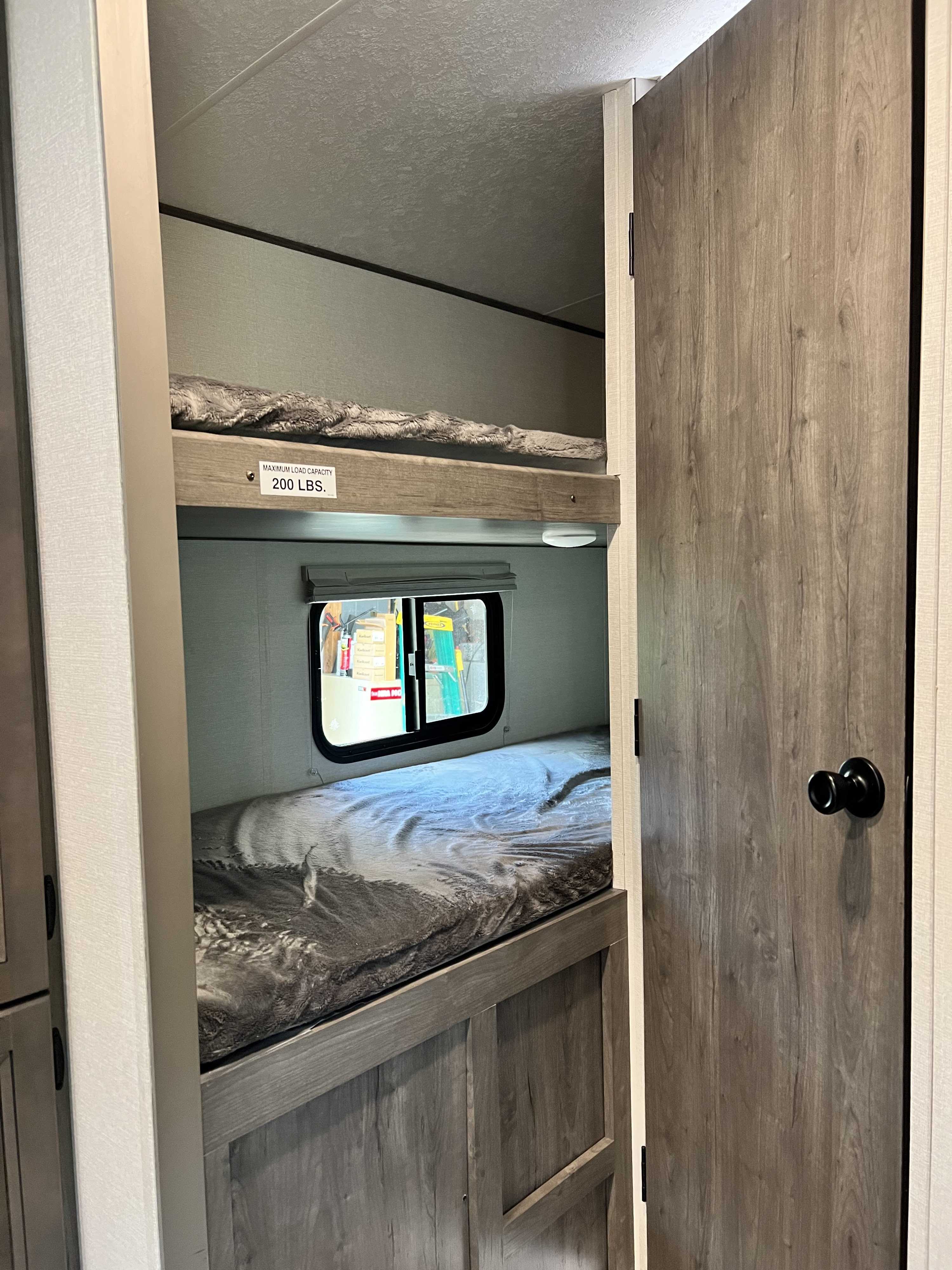 RV rental interior: bunk beds with a 200 lbs capacity sign. A window and a door are visible inside.. Coachmen Apex Nano 2021