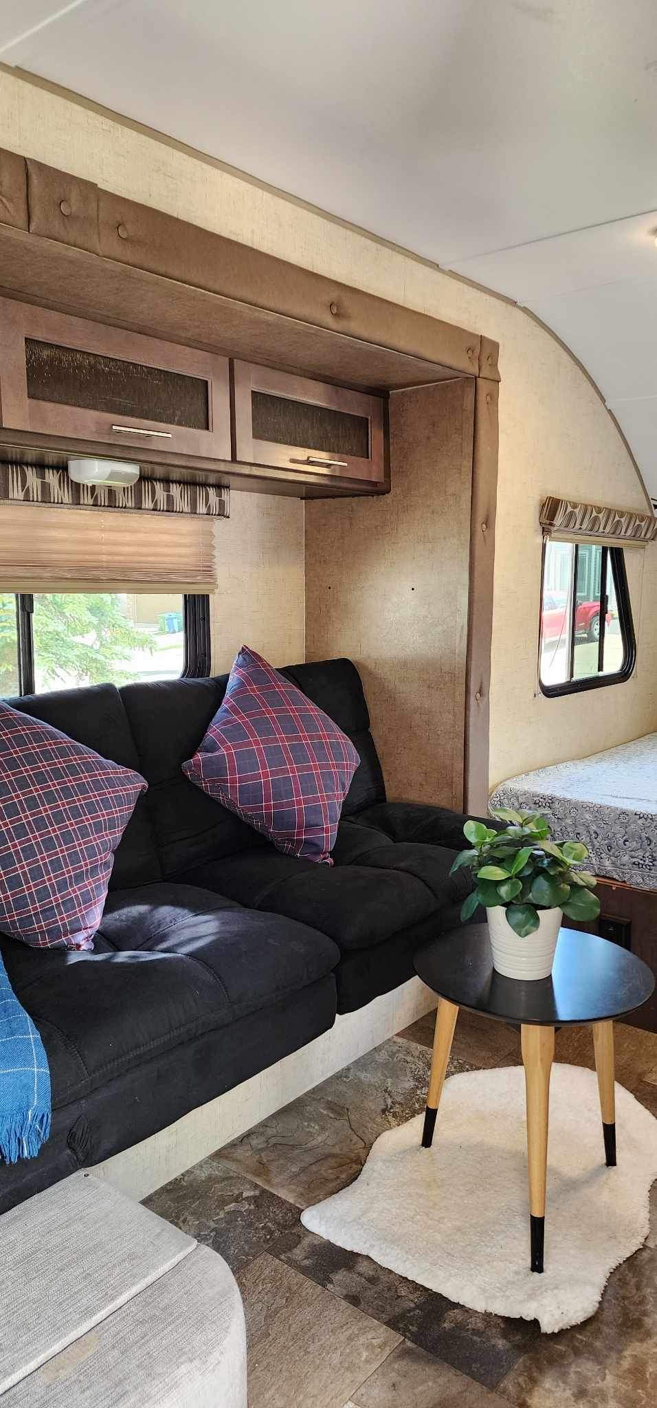 Experience a comfy **rv rental** with a black sofa, plaid pillows, side table with plant, overhead cabinets, and scenic window views.. Winnebago MicroMini 2306 BHS 2020