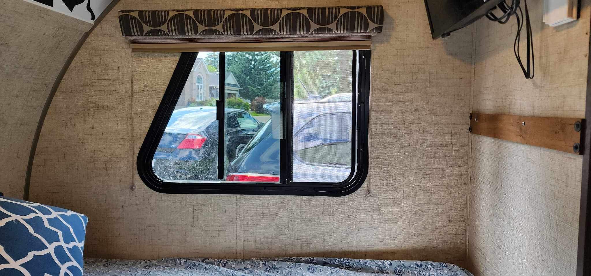 Cozy rv rental interior: a window with a view of cars and a house. Textured walls, patterned bed, and wall-mounted TV.. Winnebago MicroMini 2306 BHS 2020