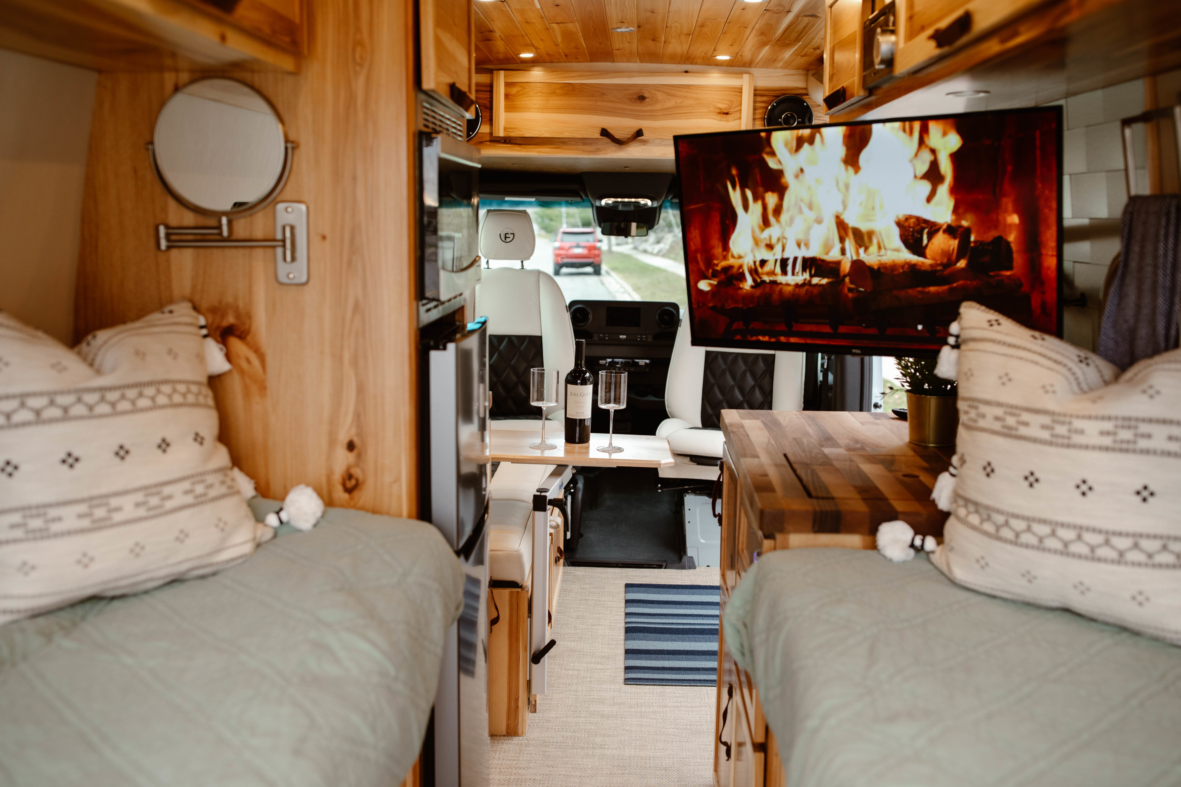 Cozy RV rental interior with wood finishes, fireplace TV, wine, and comfortable seating. Ideal for mobile travel.. Mercedes-Benz Sprinter 170 4x4 2022