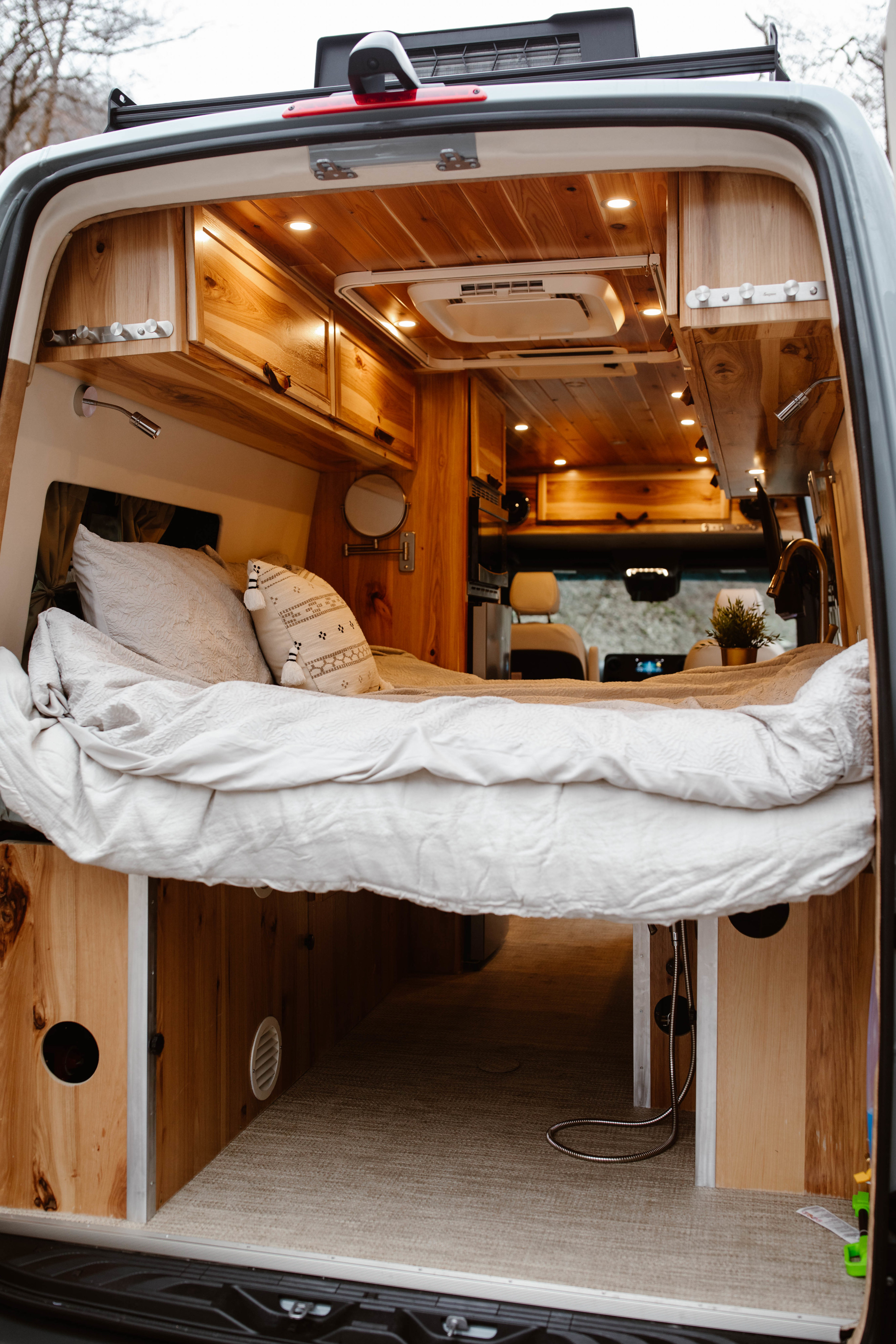 Cozy RV rental van interior: a comfortable bed, warm wood paneling, overhead lighting, and storage.. Mercedes-Benz Sprinter 170 4x4 2022