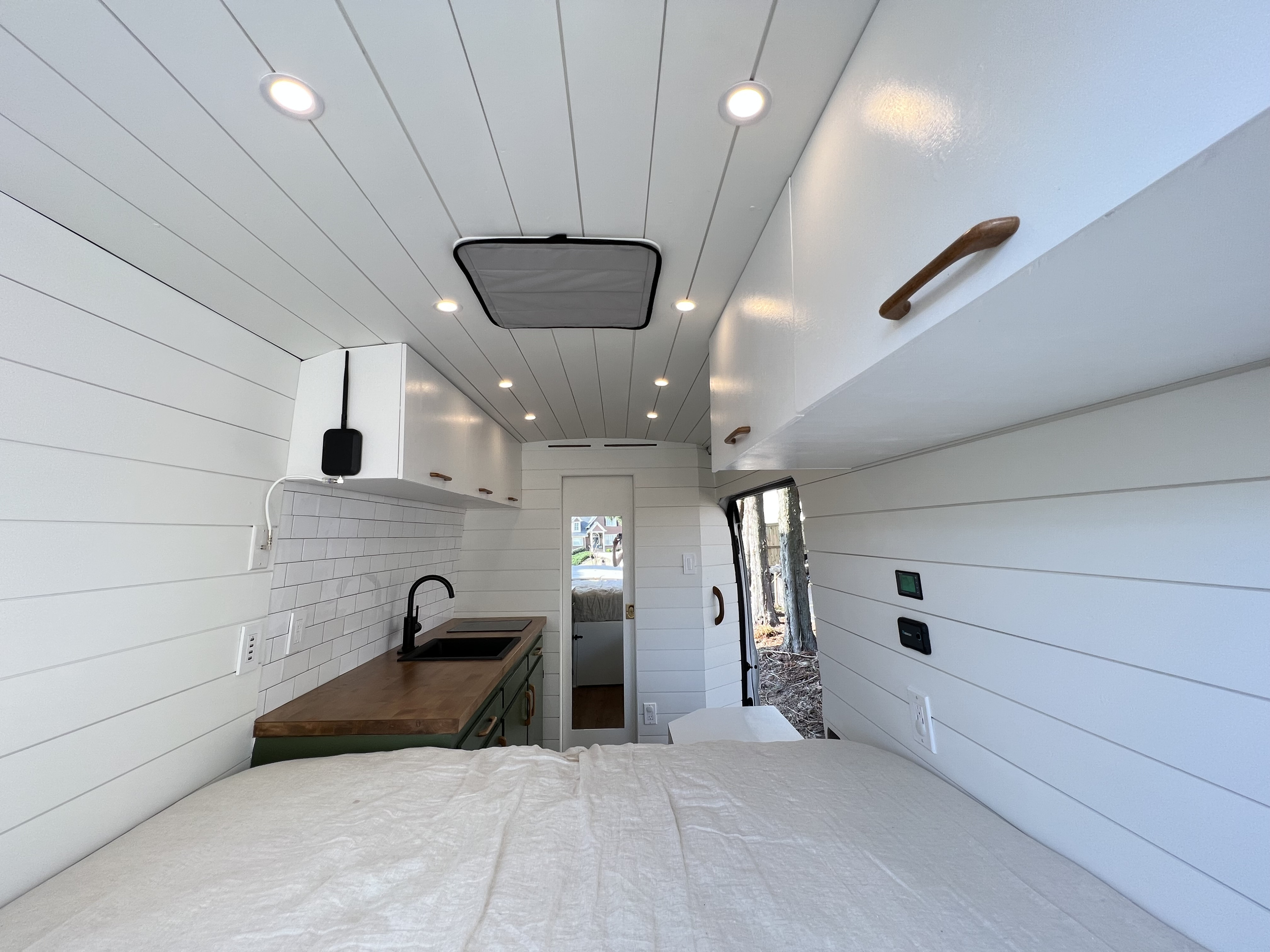 Modern rv rental interior showcasing a compact kitchen with wood counters, a comfortable bed, and clean white shiplap walls.. Ford Transit 2020
