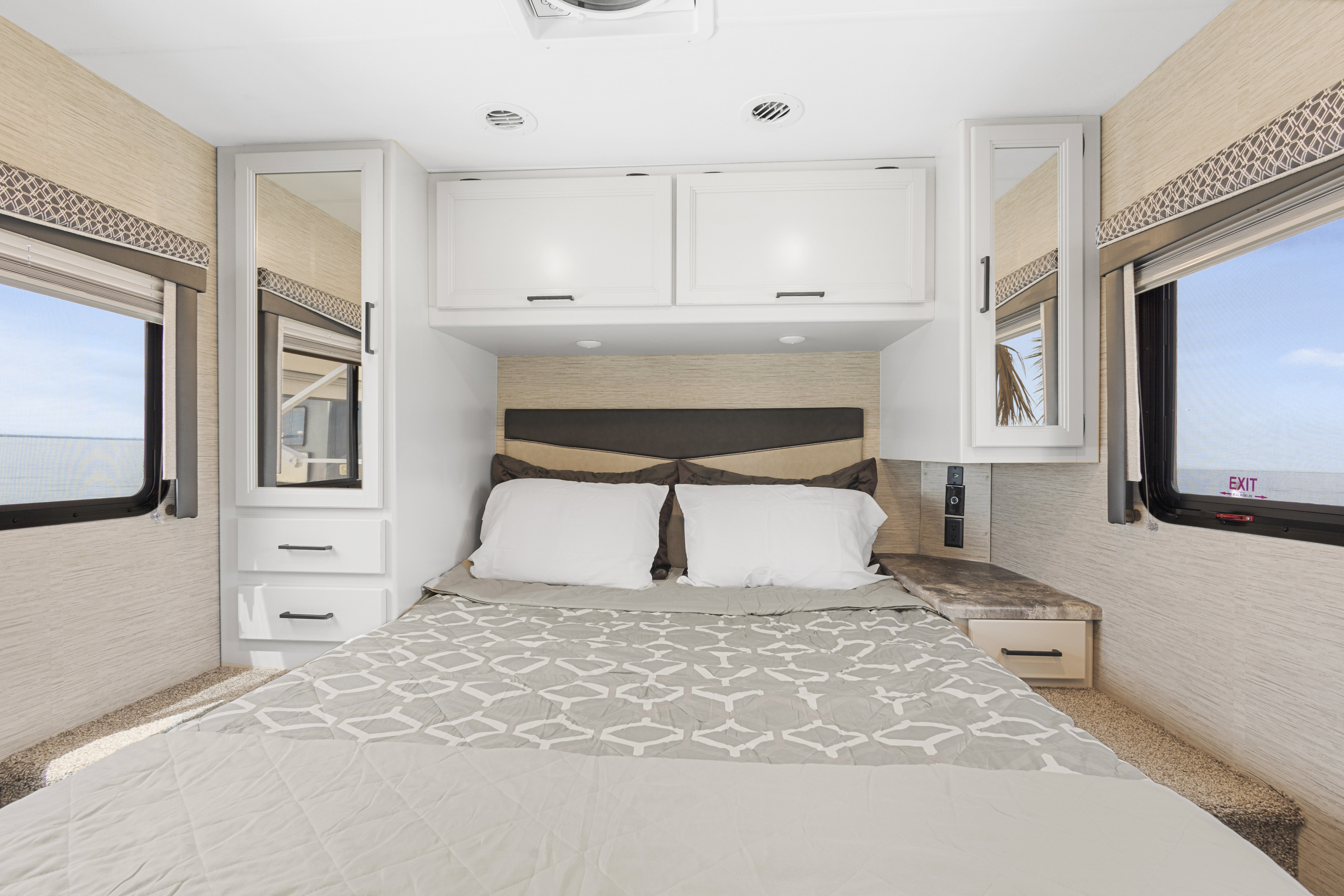 Comfortable RV rental bedroom featuring a full bed, white overhead storage, and mirrored side cabinets with windows.. Thor Four Winds 2023