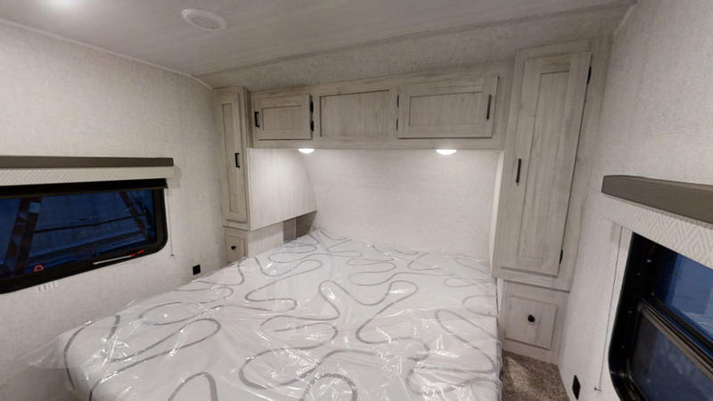 Modern RV rental bedroom interior features a light-toned bed, overhead and side cabinets, and windows, ready for your adventure.. East to West Della Terra 2023