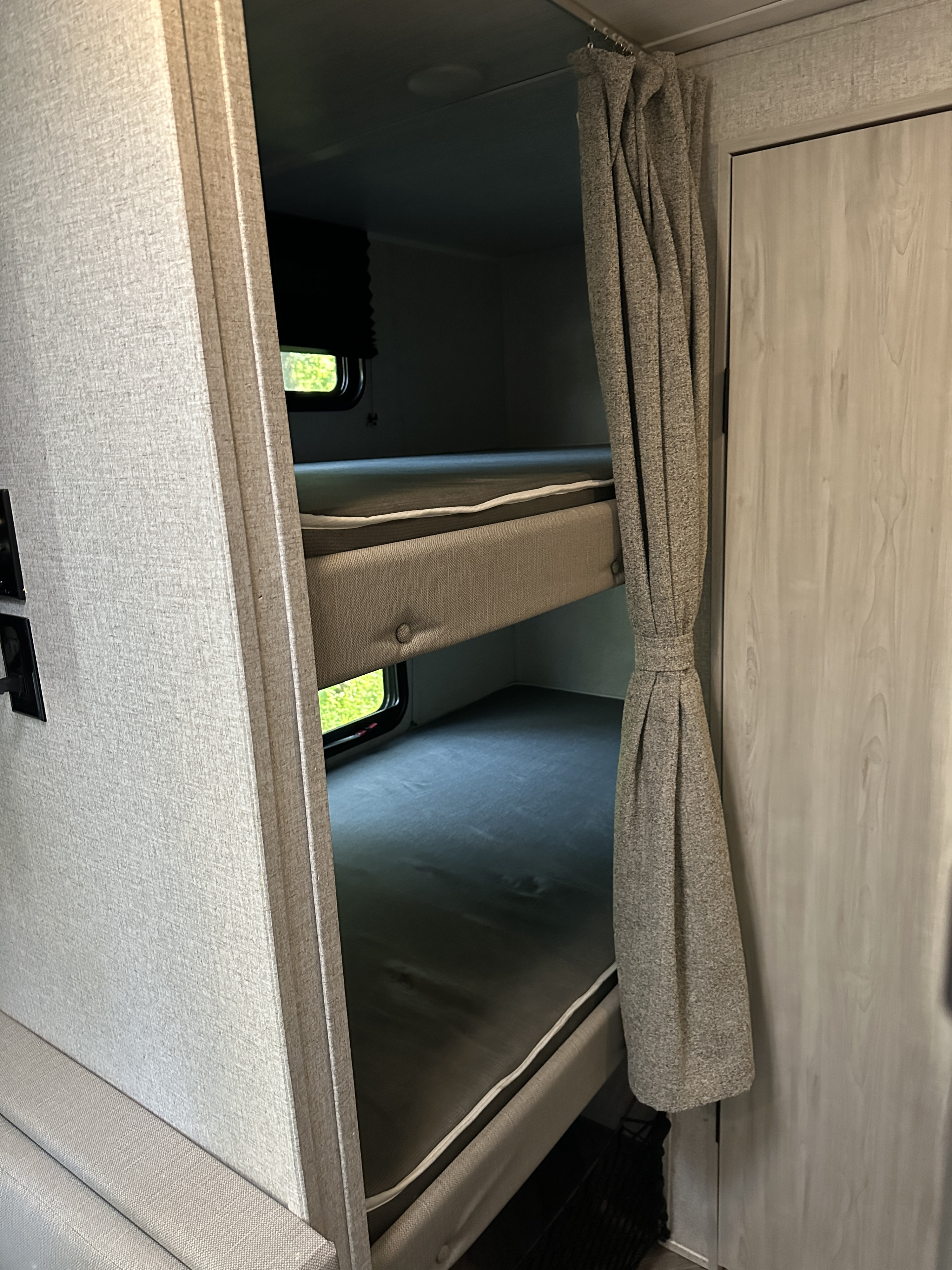 Cozy RV rental bunk beds with privacy curtains. This RV interior offers comfortable sleeping for travelers.. East to West Della Terra 2023