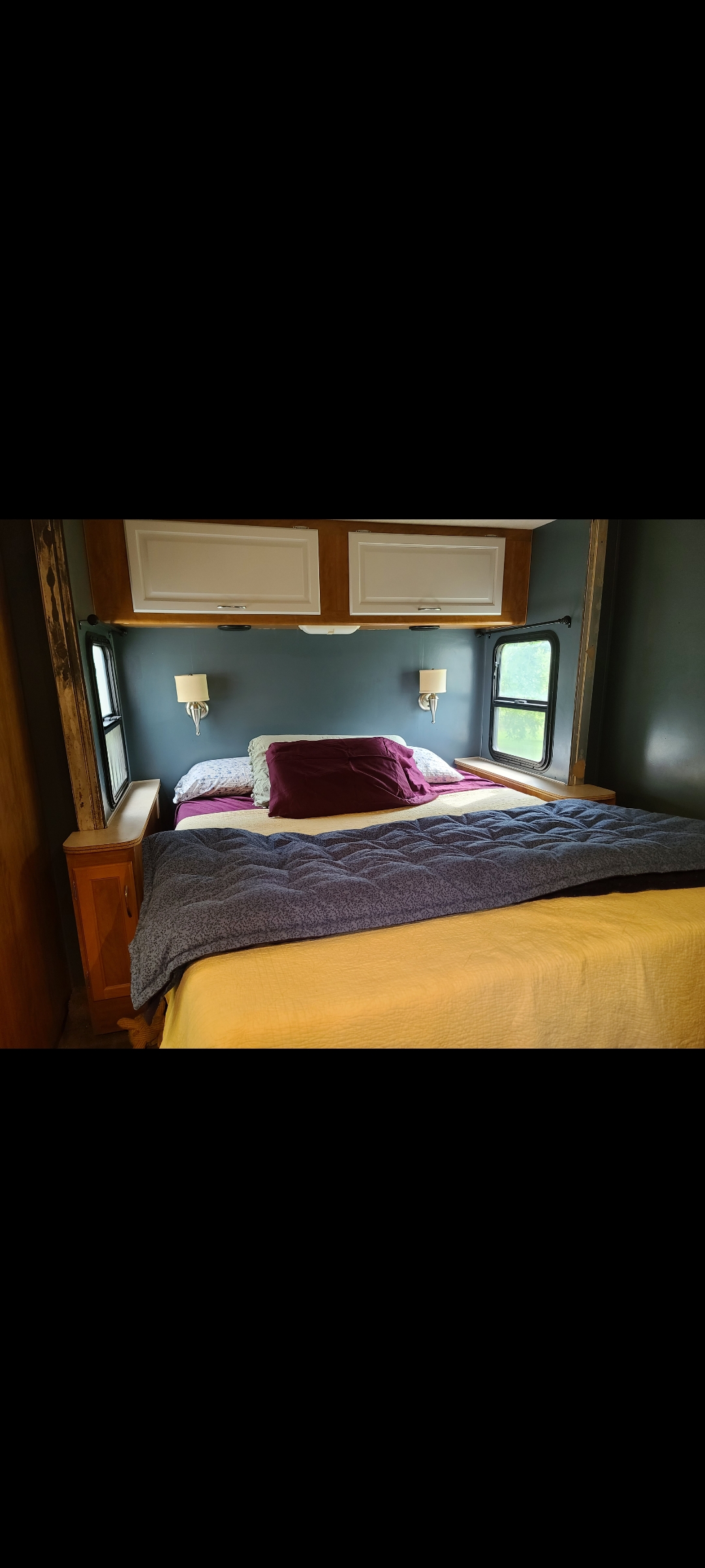 Cozy RV rental bedroom with a neatly made bed in yellow and purple, wall-mounted lamps, and overhead storage.. Fleetwood Other 2006