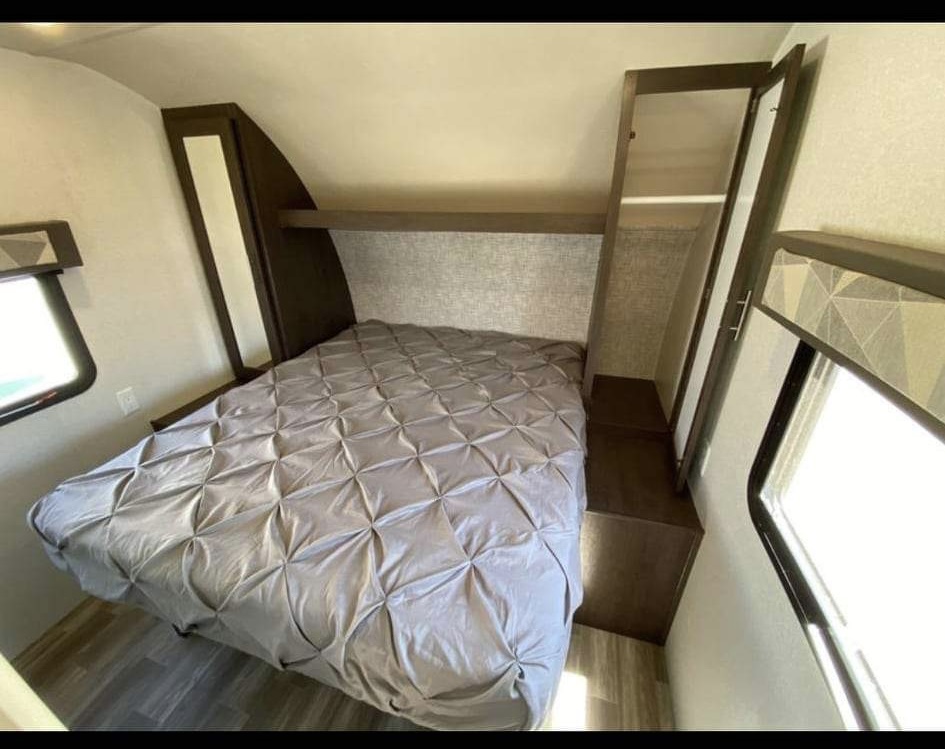 Comfortable RV rental bedroom featuring a gray bed, built-in storage, and windows. Ideal for road trip adventures.. Forest River Salem 2019