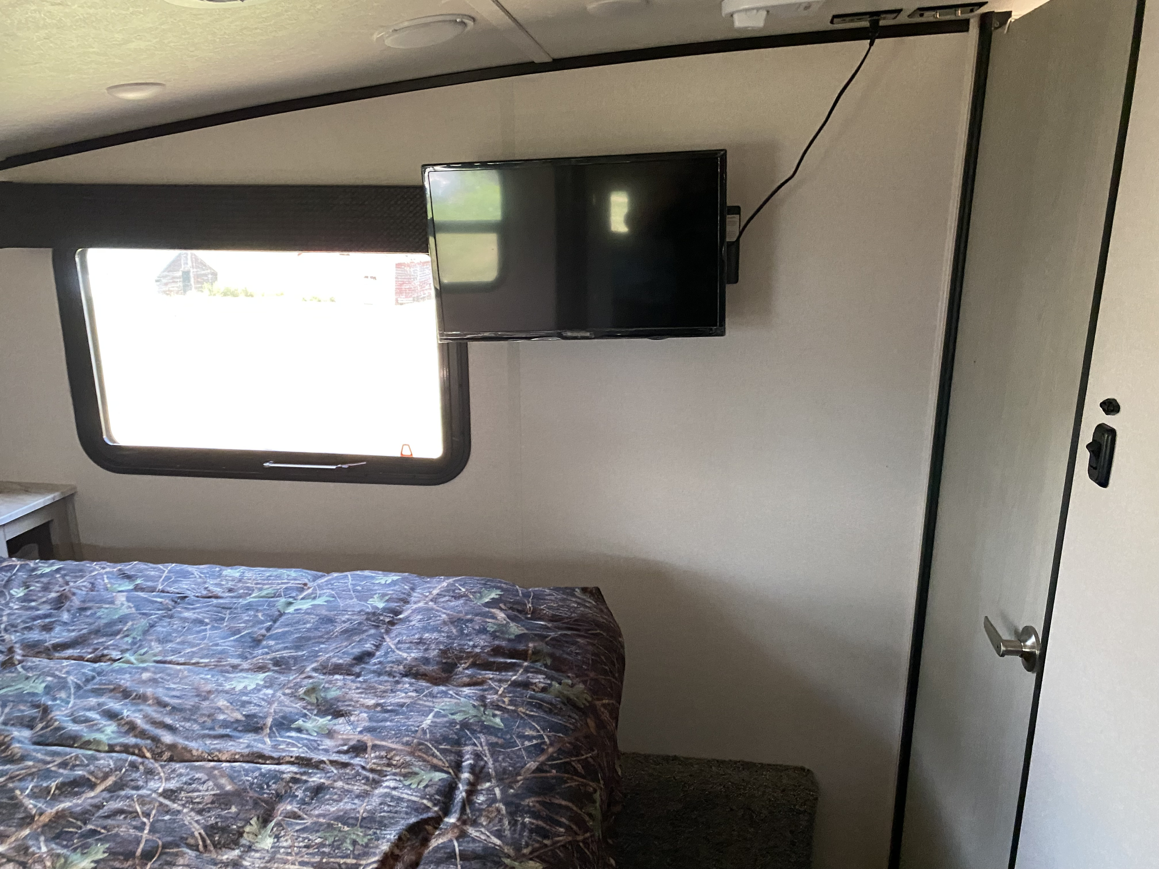 Cozy RV rental bedroom featuring a mounted TV, a window with an outdoor view, and a camo comforter.. Forest River Coachmen Chaparral X-Lite 2018